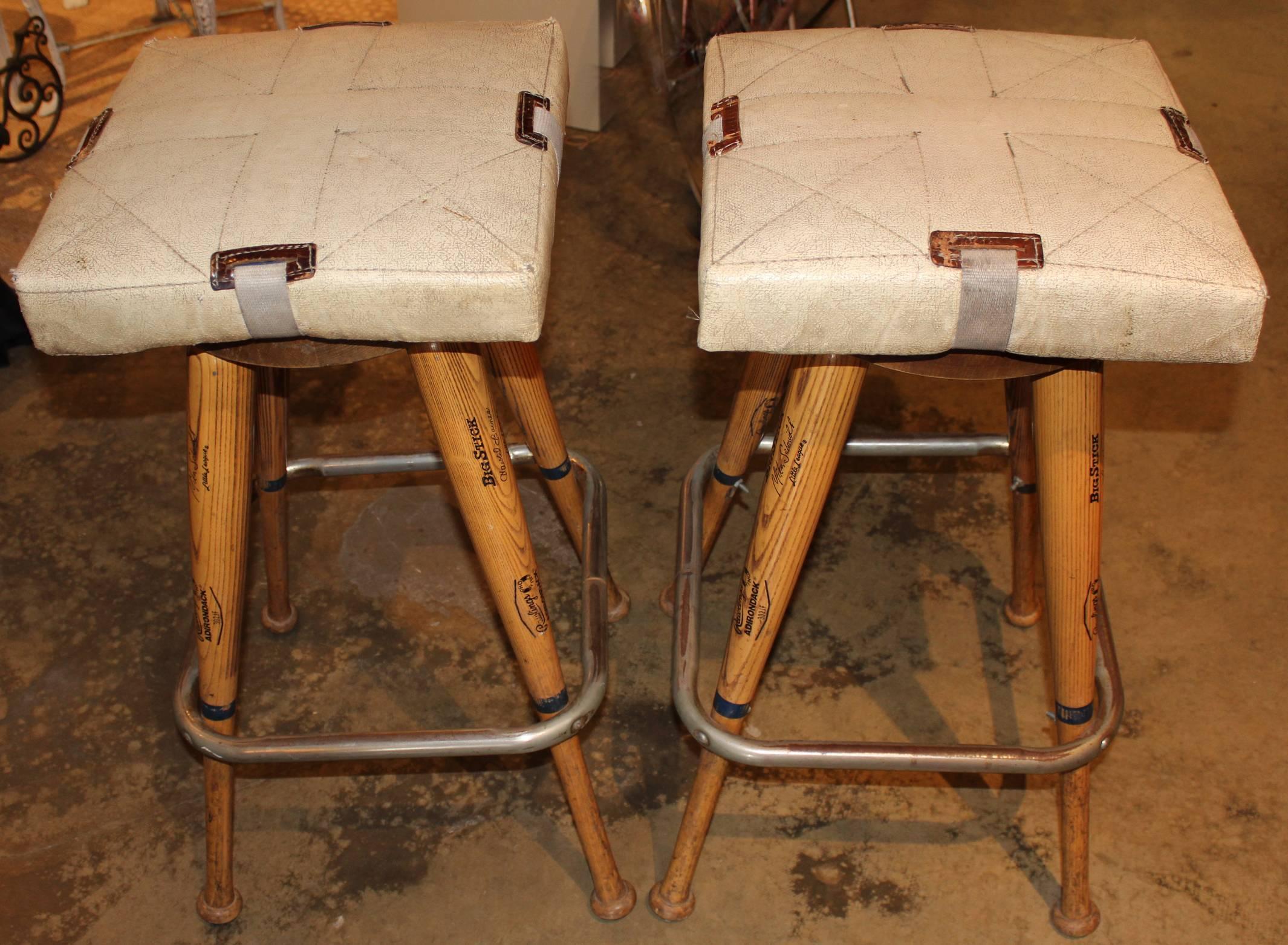 A wonderful custom pair of bar stools constructed with baseball bat legs and actual bases for seat pads, each attached to a round wooden seat. The bats used are rawlings adirondack pro ring big stick little league bats with several 1980s pro