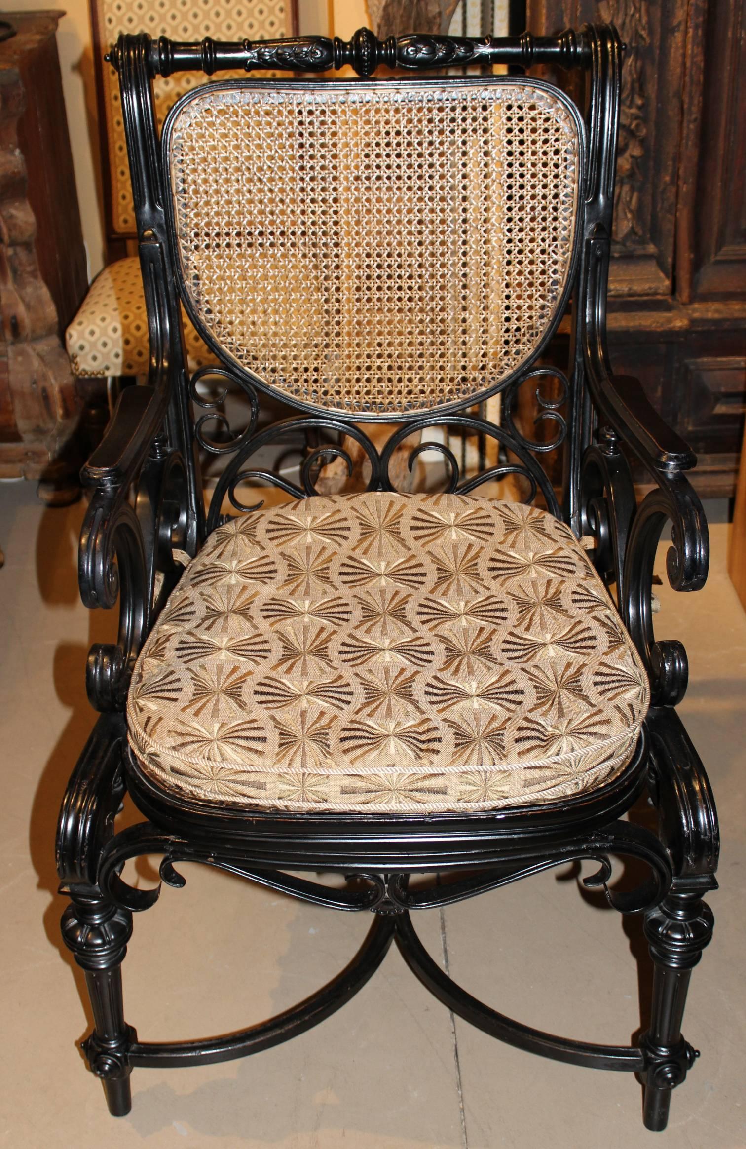 A well crafted Aesthetic ebonized bentwood armchair of pleasing proportion with caned seat and back, scroll carved decoration, turned crest rail, and demilune bentwood stretchers. A freshly upholstered cushion has been added to accent the piece.