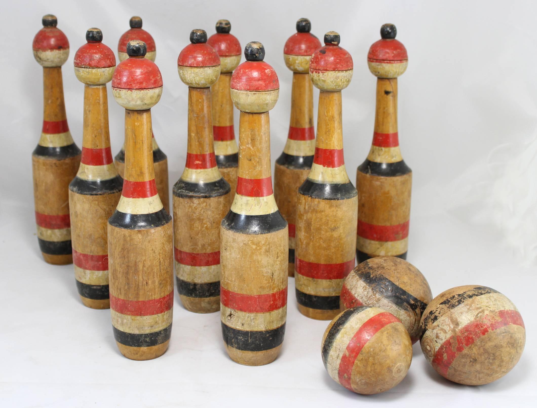 An antique set of ten lawn bowling skittles with three balls, each turned and hand-painted in red, white and deep blue (possibly black) striping. They have great patina, minor imperfections, shrinkage cracks, and expected wear from age and use.