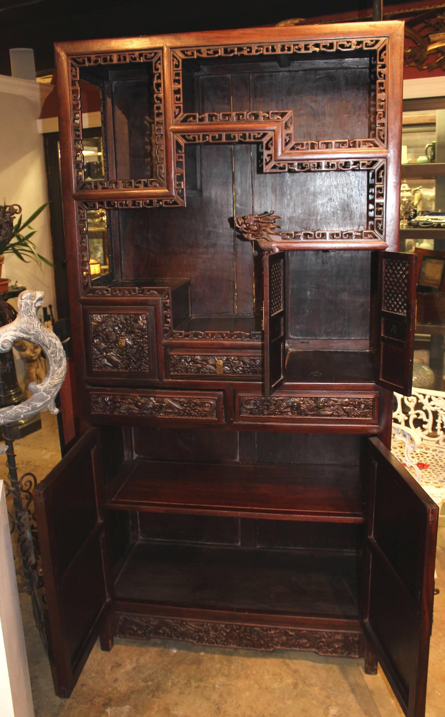 A splendidly carved pair of carved Chinese rosewood etageres or collectors cabinets, each with a combination of open and closed compartments, some with carved panel doors and others with carved drawer fronts, and each with two large heavily carved