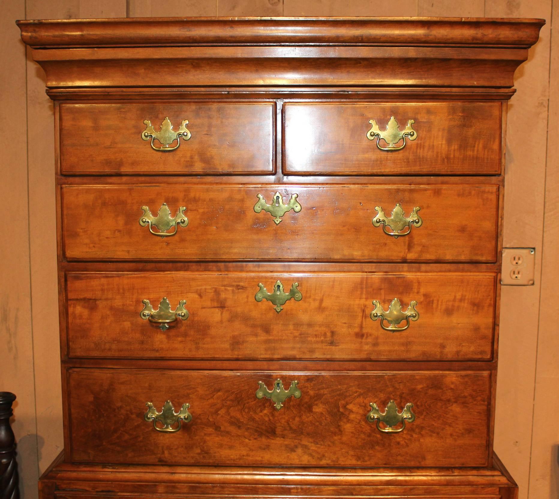 A two part flat top 18th century Queen Anne highboy in a warm toned maple of New England origin, with molded cornice concealing a secret long drawer surmounting an upper case with two short drawers over three long drawers and a lower case with waist