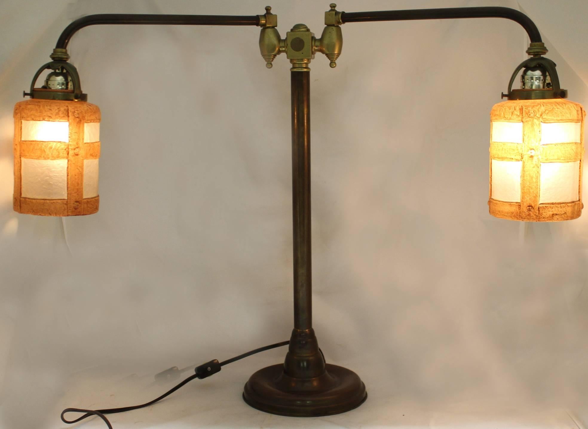A splendid Arts and Crafts double student lamp, with two adjustable arms and chipped ice glass shades, each embossed Handel near the top rim, the base signed Handel at the top brass fixture. The lamp sockets have been replaced, and the lamp is in
