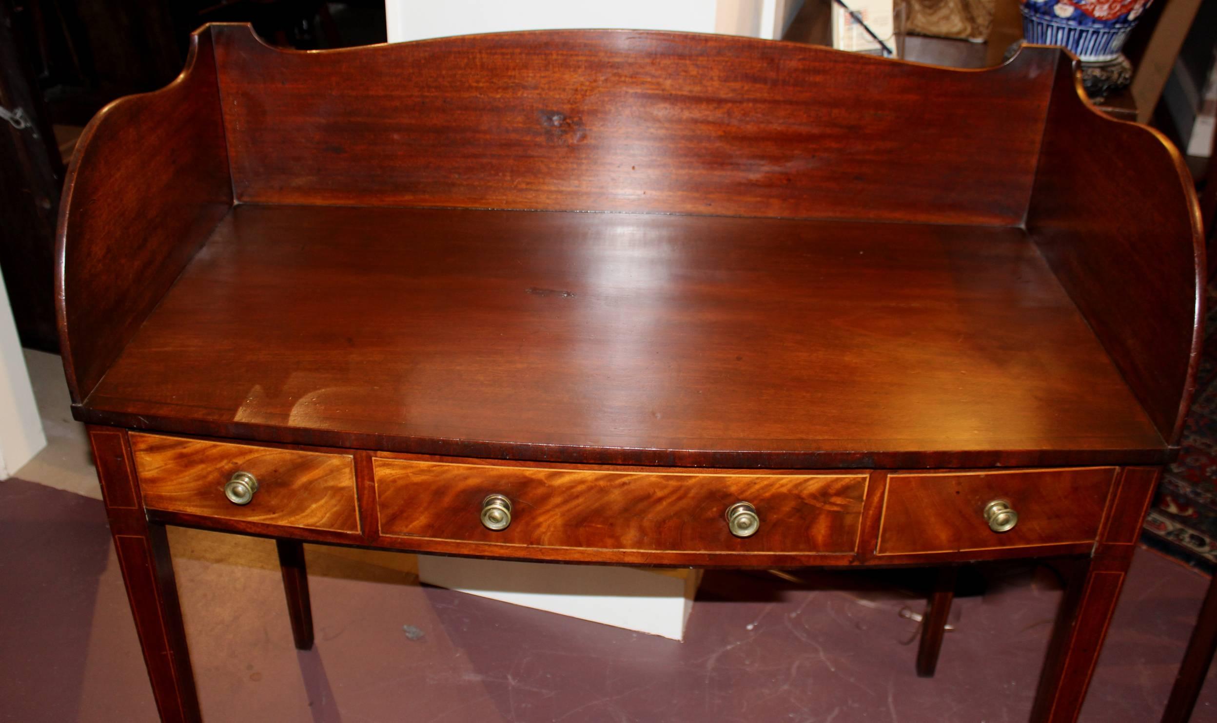 A fine mahogany bow front mahogany server with nicely shaped splash rail and delicate line inlay, two fitted small drawers flanking a center false drawer, all supported with four square tapered legs. The brasses appear to be original to the piece.