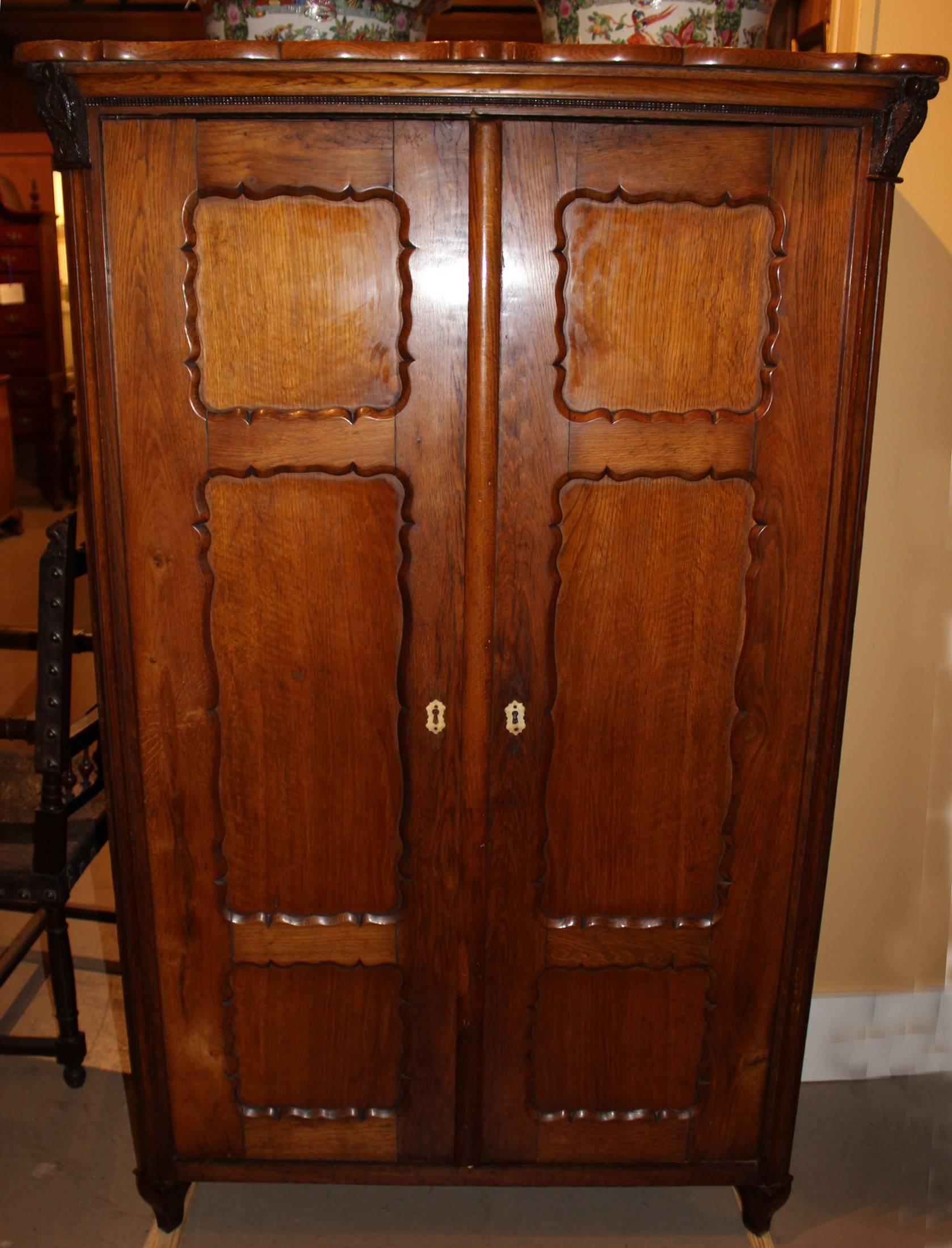 A diminutive size French fruitwood armoire in a warm brown finish, with shaped top over two tri-paneled doors flanked by canted fluted columns with carved owl capitals, all supported by two front shaped feet and rear block feet. Dates to the 19th