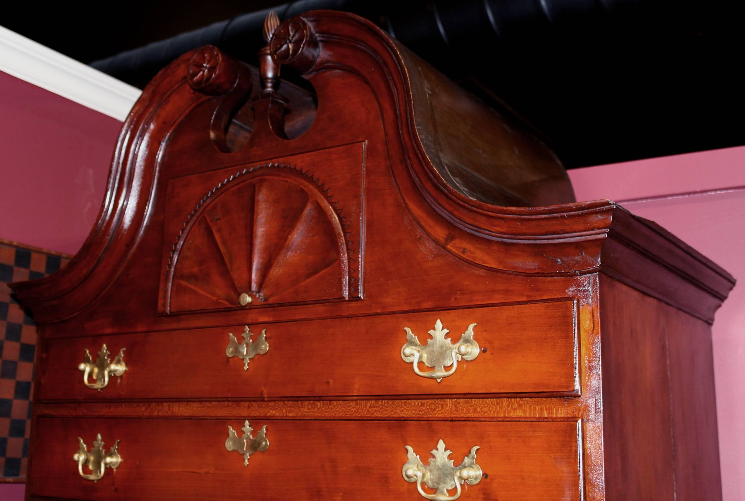 This exceptional cherry chest on chest with split pediment bonnet top with rosettes, flame finials, an upper case with a center deep drawer with a spectacular radial fan carved front, over five graduated long drawers, a lower case with three long