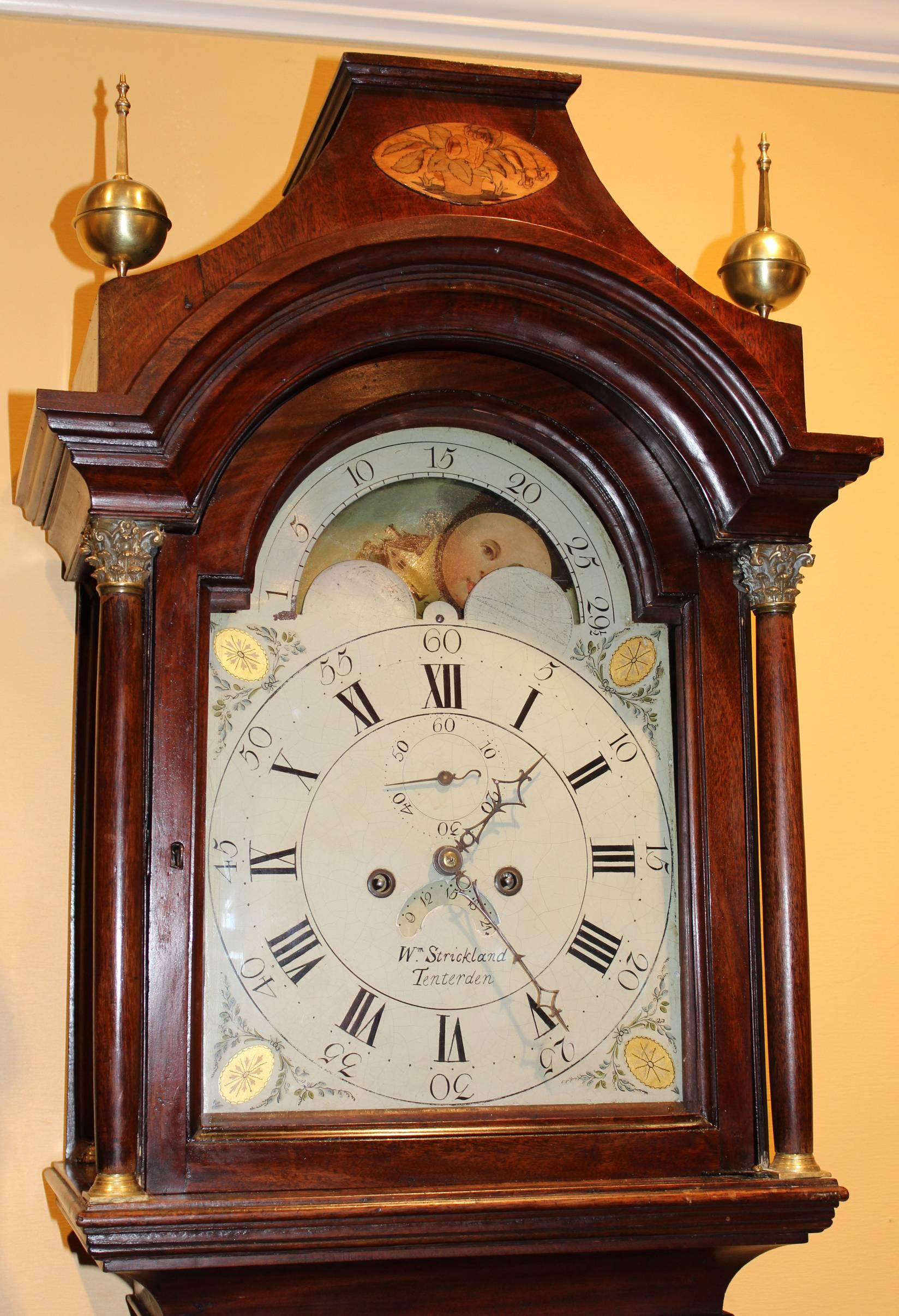 A fine English mahogany tall case clock with inlaid mahogany crest, brass ball and spire finials. Painted arched metal dial with nicely executed moon phase, Roman and Arabic numerals, seconds and date aperture, spandrels with wreaths and gilded