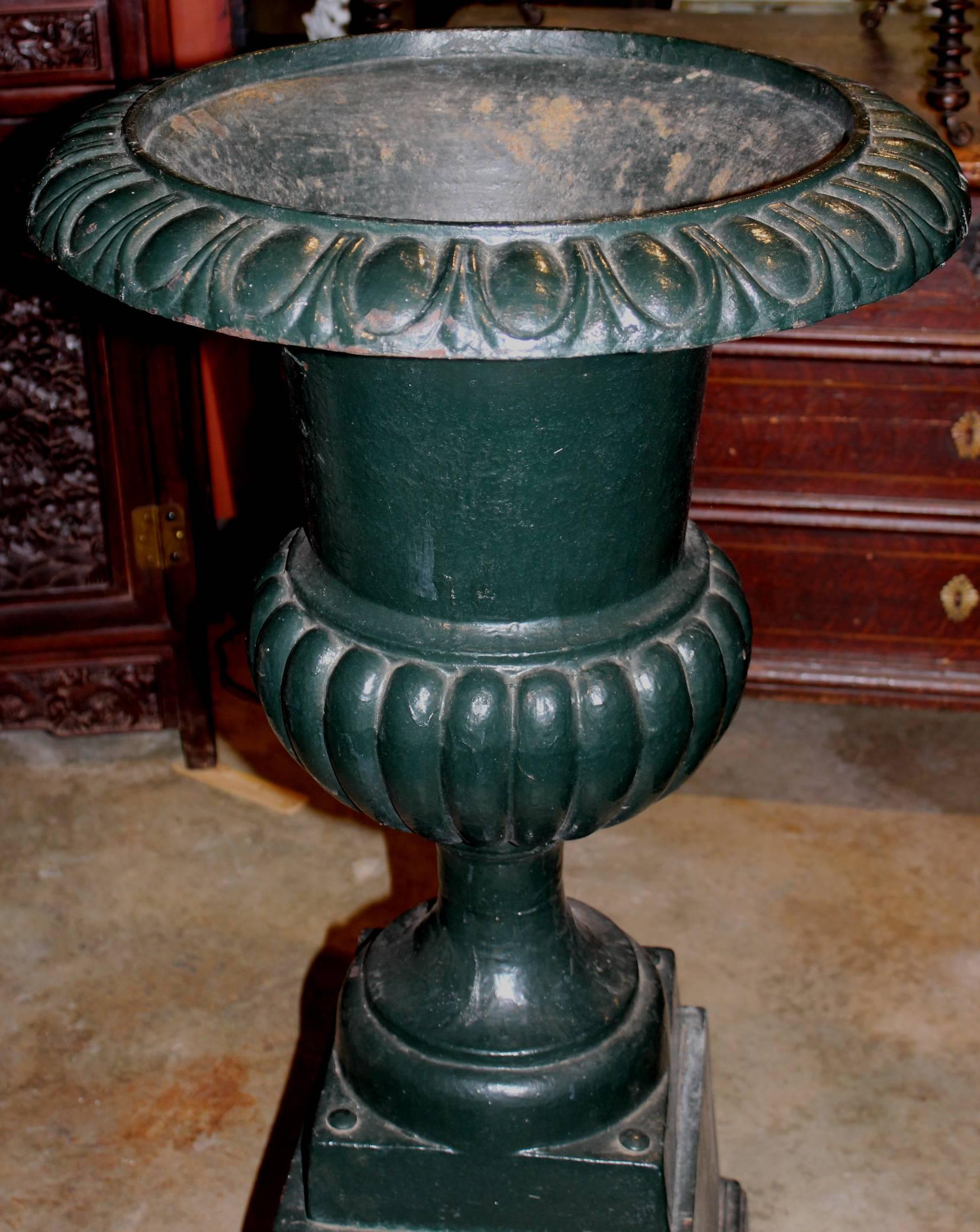 A fine pair of Classic form Victorian iron urns in green paint with attached bases. A great addition to your garden or patio decor! Very good overall condition, with some minor paint losses, and rust visible on the bases.