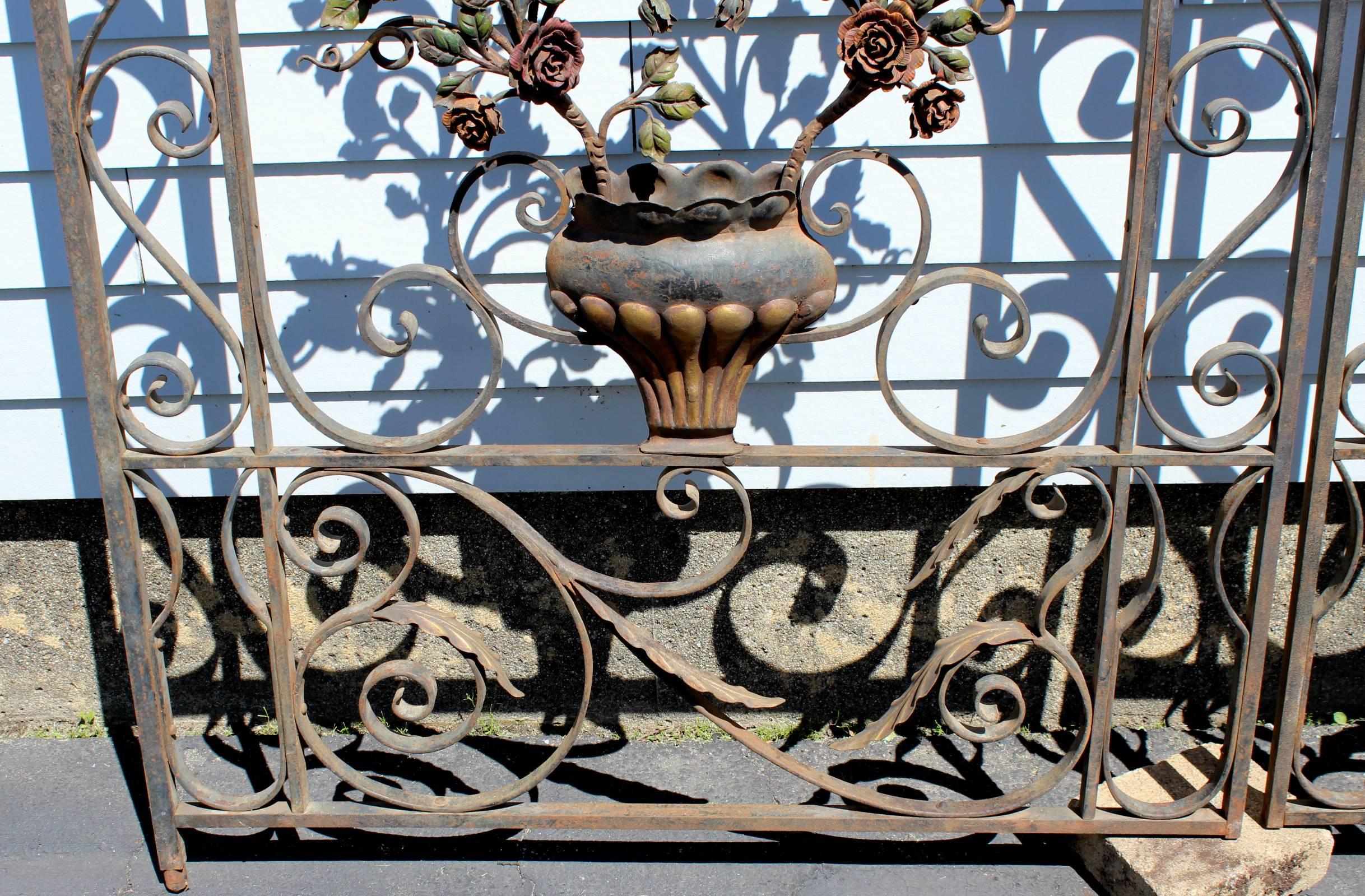An exceptional pair of polychrome iron garden gates with a center three dimensional urn with spray of roses decoration on each door, surrounded by detailed iron scrollwork. Each door has an attached hinge mount on the upper corner. Very good overall