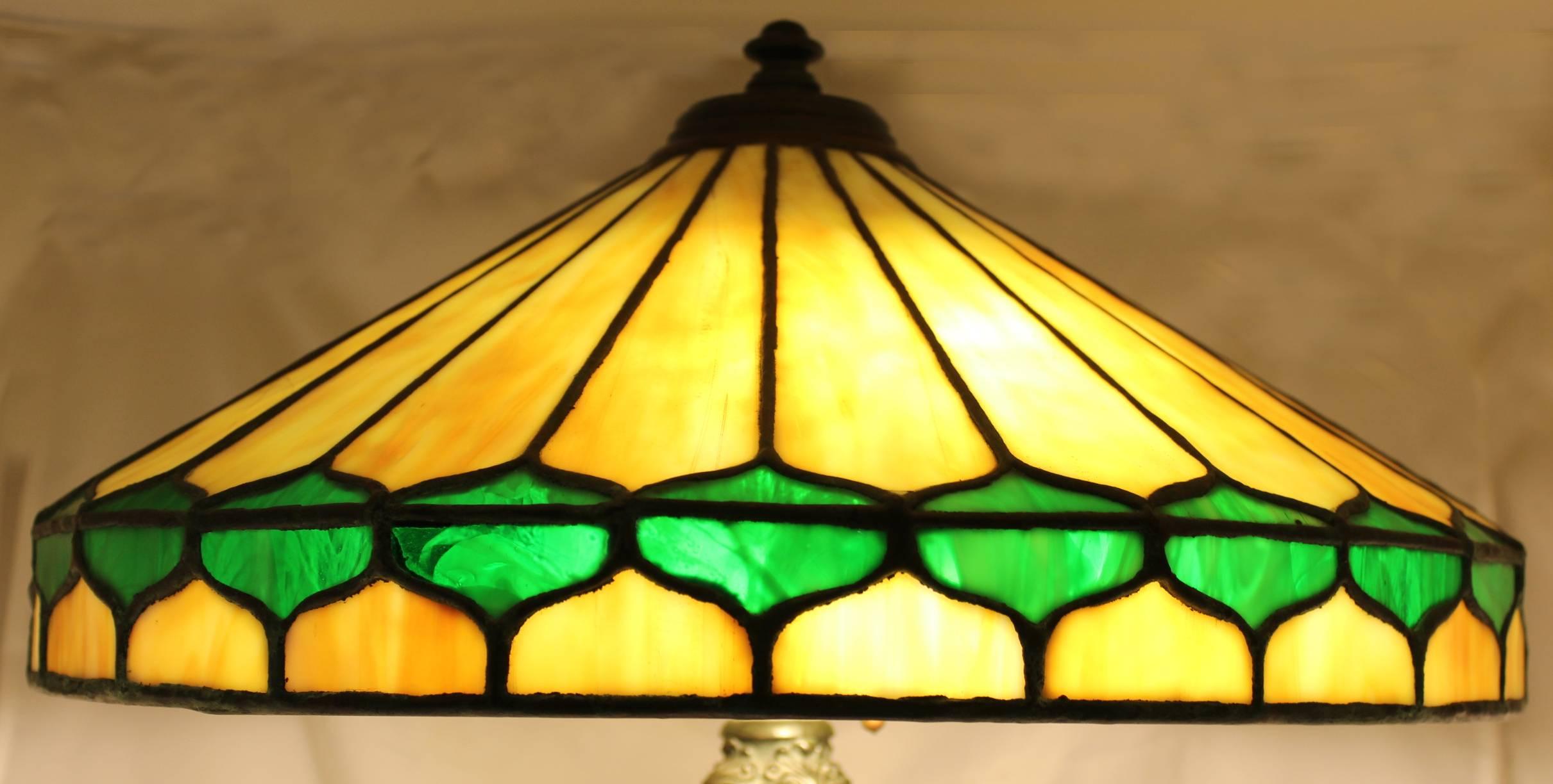 A fine 24 panel leaded glass Arts & Crafts three light table lamp with warm yellows and greens, with scrolled cast metal foliate decorated footed base, marked with 515 embossed, Excellent overall restored working condition, with recent wiring and