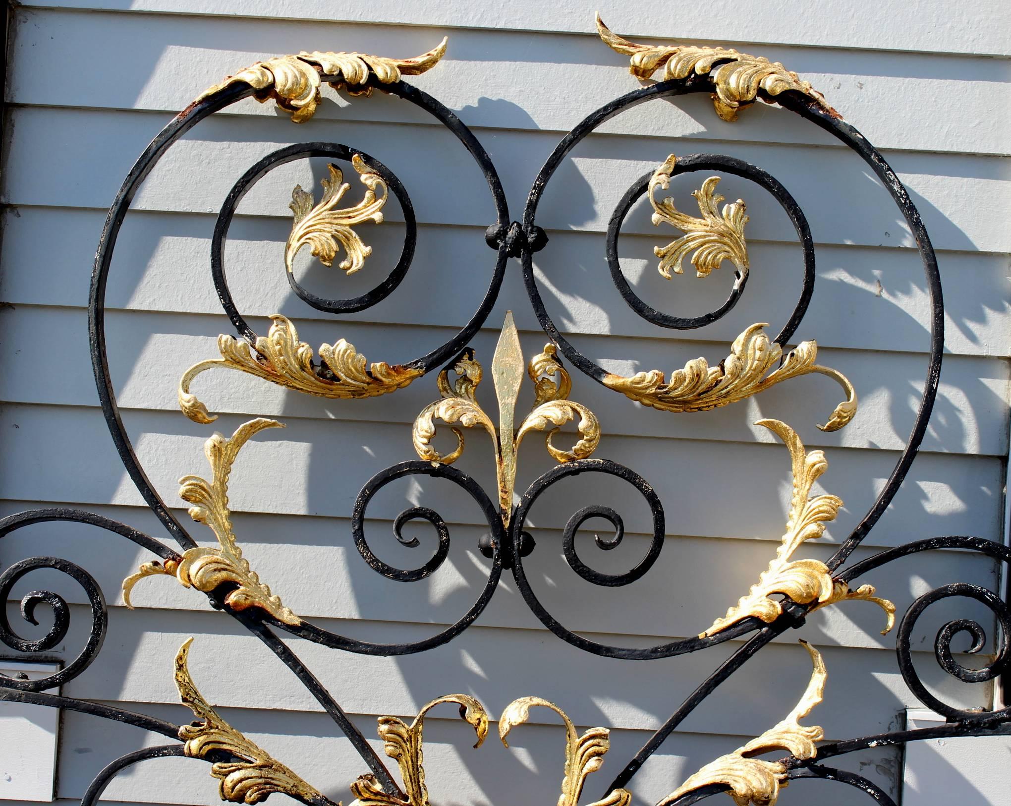 A monumental Victorian iron gate crest in black with exceptional scrollwork and gilt applied foliate highlights, including two rosettes, a central heart, and a fleur-de-lis, all surmounting a small circular central scroll decoration between the