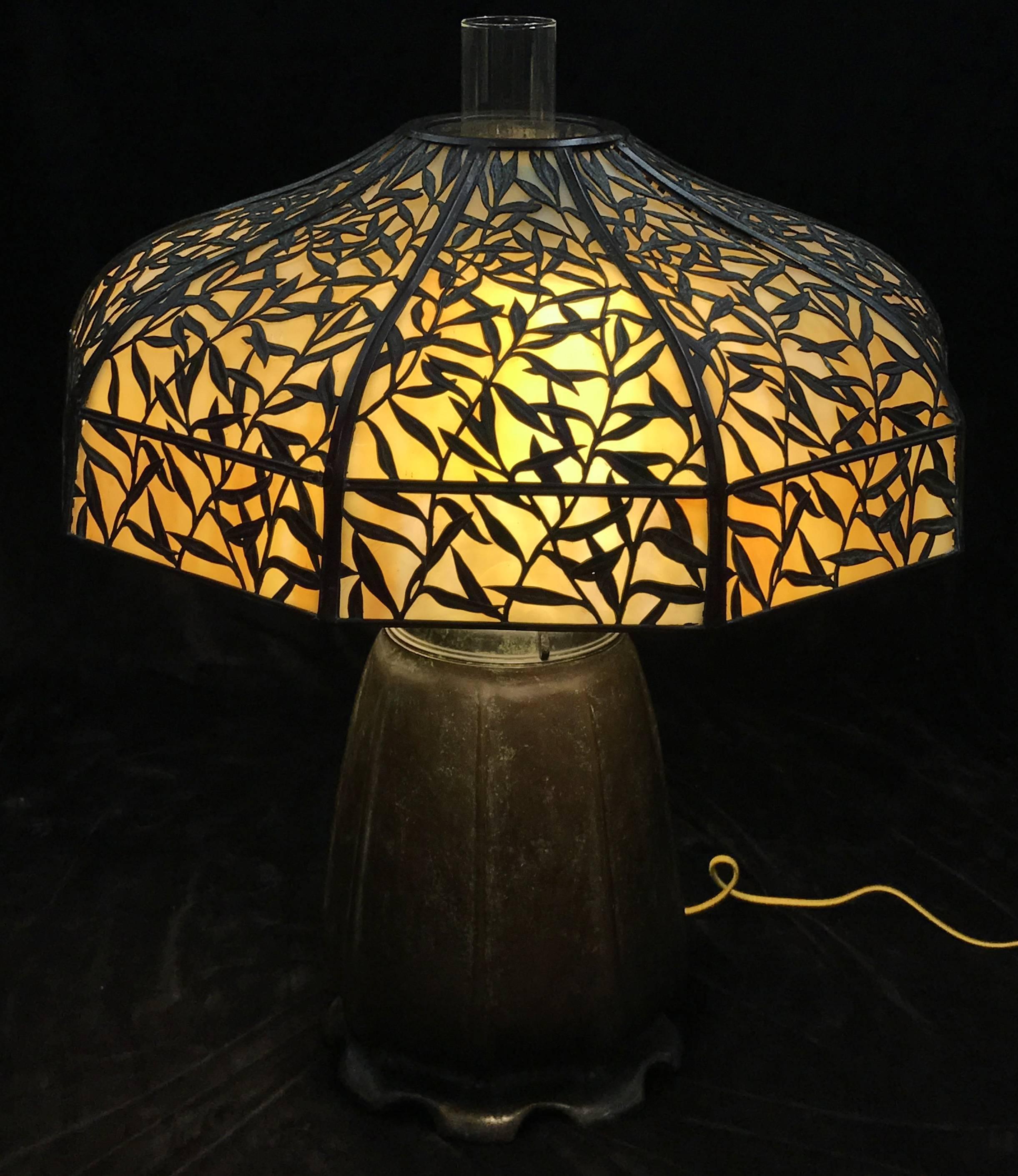 An exquisite Art Nouveau / Arts & Crafts 18 panel slag glass table lamp with metal bamboo overlay on the shade, supported by a large patinated bronze base signed Handel on the font and bottom. The lamp has retained its original oil components