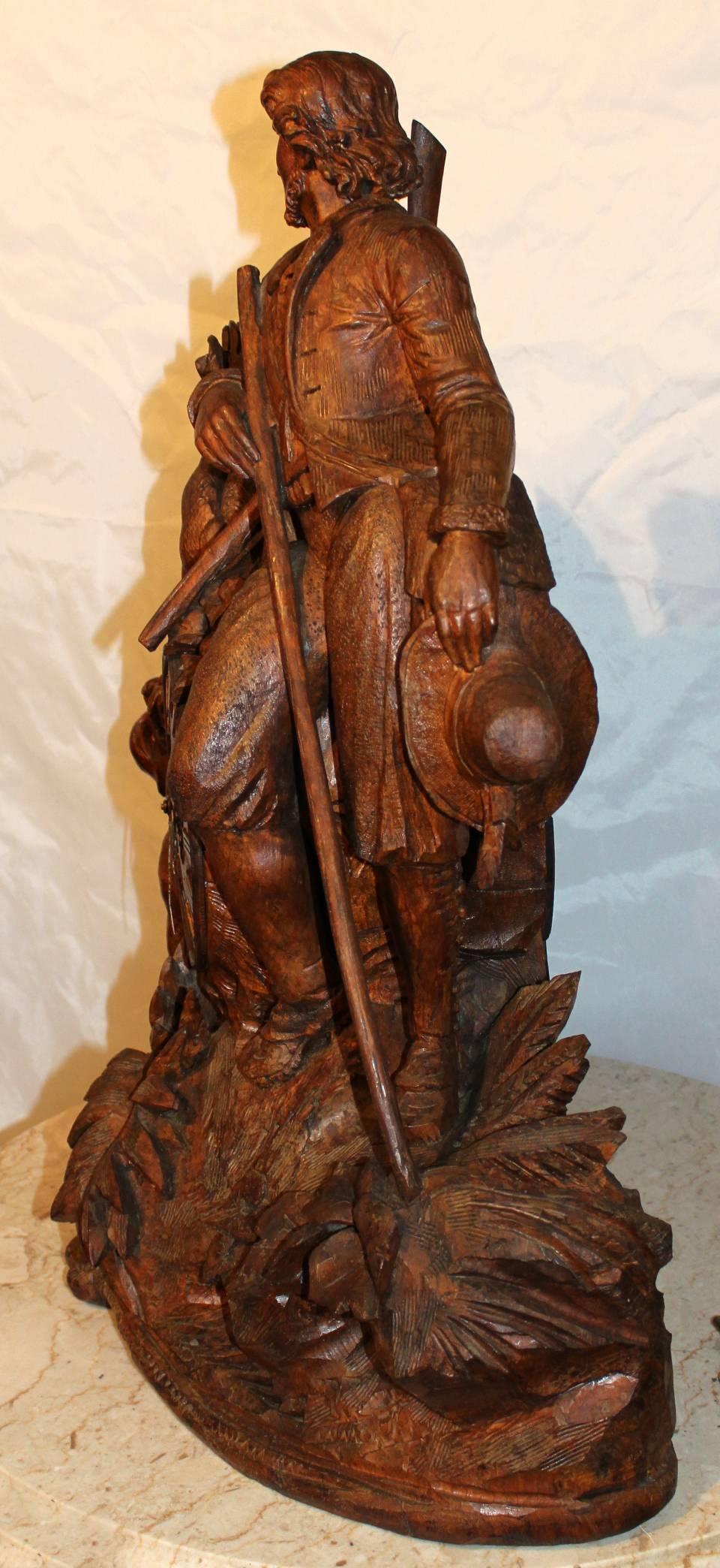A monumental carved walnut black forest mantel or shelf clock sporting / hunting motif. Featuring a hunter with a long rifle or musket slung over his shoulder under his right arm, hat in hand, with hunting dog and his latest deer, resting on a log