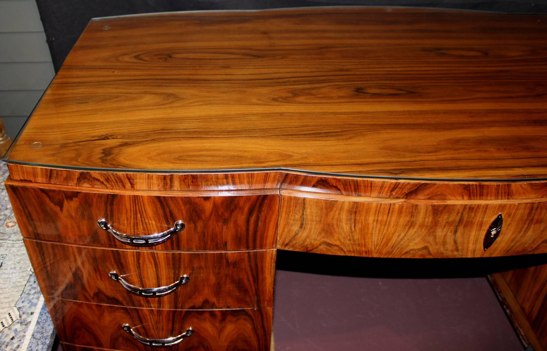 A fine form French Art Deco desk in a rich rosewood veneer, with custom fitted glass top over a single center drawer, four drawers on the left, and single door on the right which opens to a single shelf storage compartment or bookcase. The back of