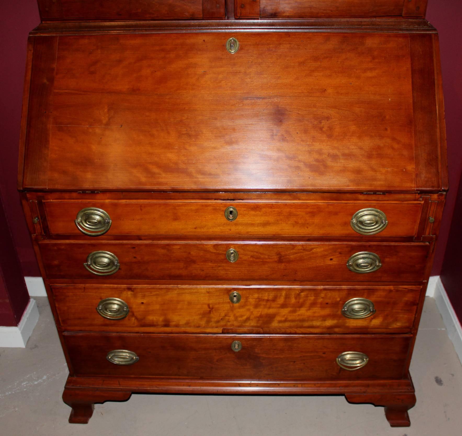 A splendid two-part cherry Chippendale secretary, its upper case with broken arched pediment flanking a central carved acorn and flame finial over two paneled doors which open to a compartmentalized shelf interior. The center divider has a custom