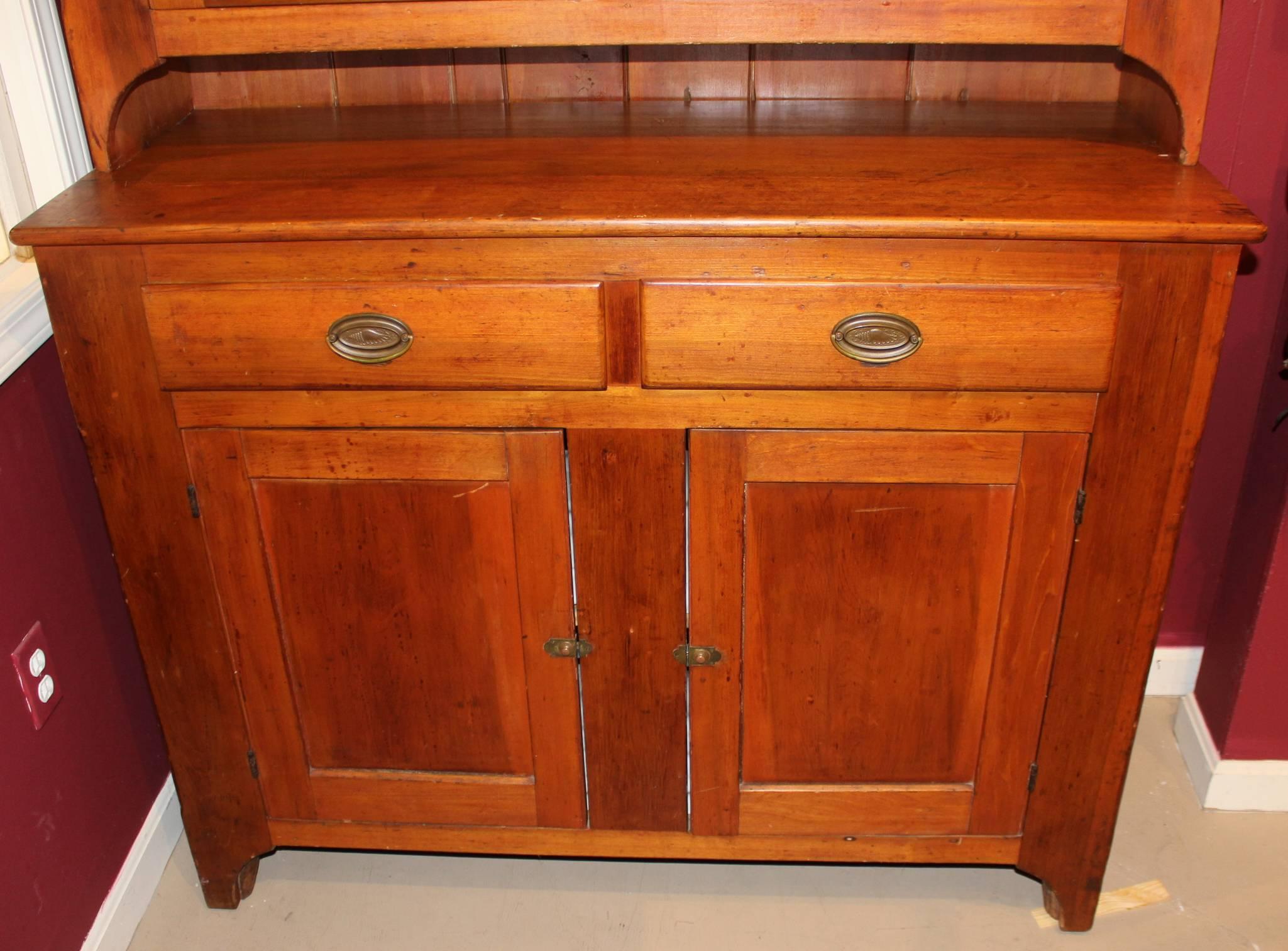A fine two-piece pine step back cupboard in old restored red wash finish, its upper case with a molded cornice over two six pane glazed doors with wavy glass panels, opening to two interior shelves with tongue and groove backing, and its lower case