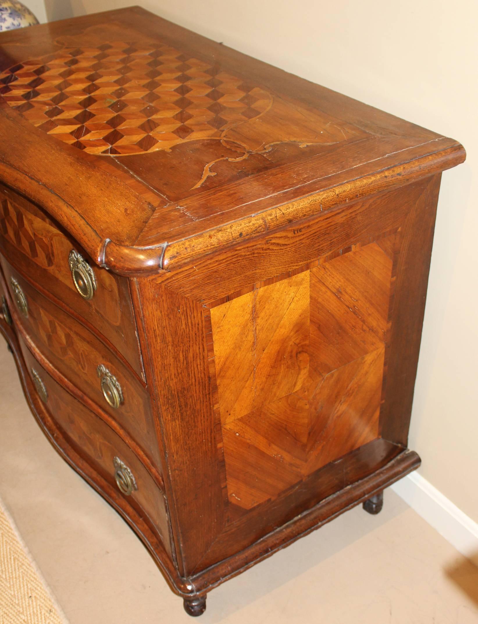A fine example of a Continental Rococo fruitwood three drawer commode with serpentine front, probably Swiss in origin, dating to the 18th century, with exceptional tumbling block parquetry on the top and drawer fronts, a molded conforming top, and