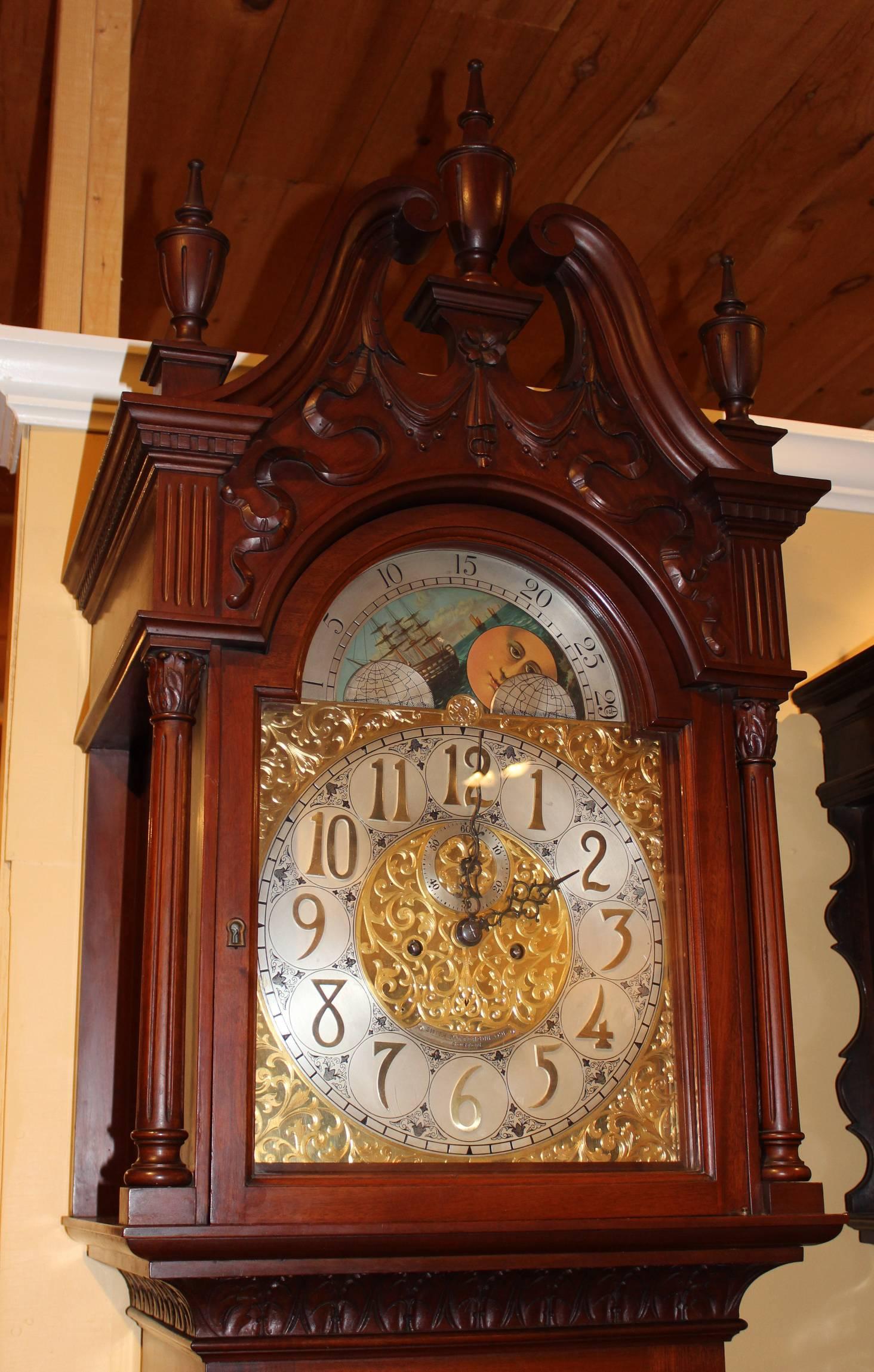 An exceptional mahogany tall case clock with single tubular chime, along with a ribbon carved bonnet with swan’s neck broken pediment, three urn finials, freestanding fluted columns flanking the dial door, 13 inch chased brass dial with applied