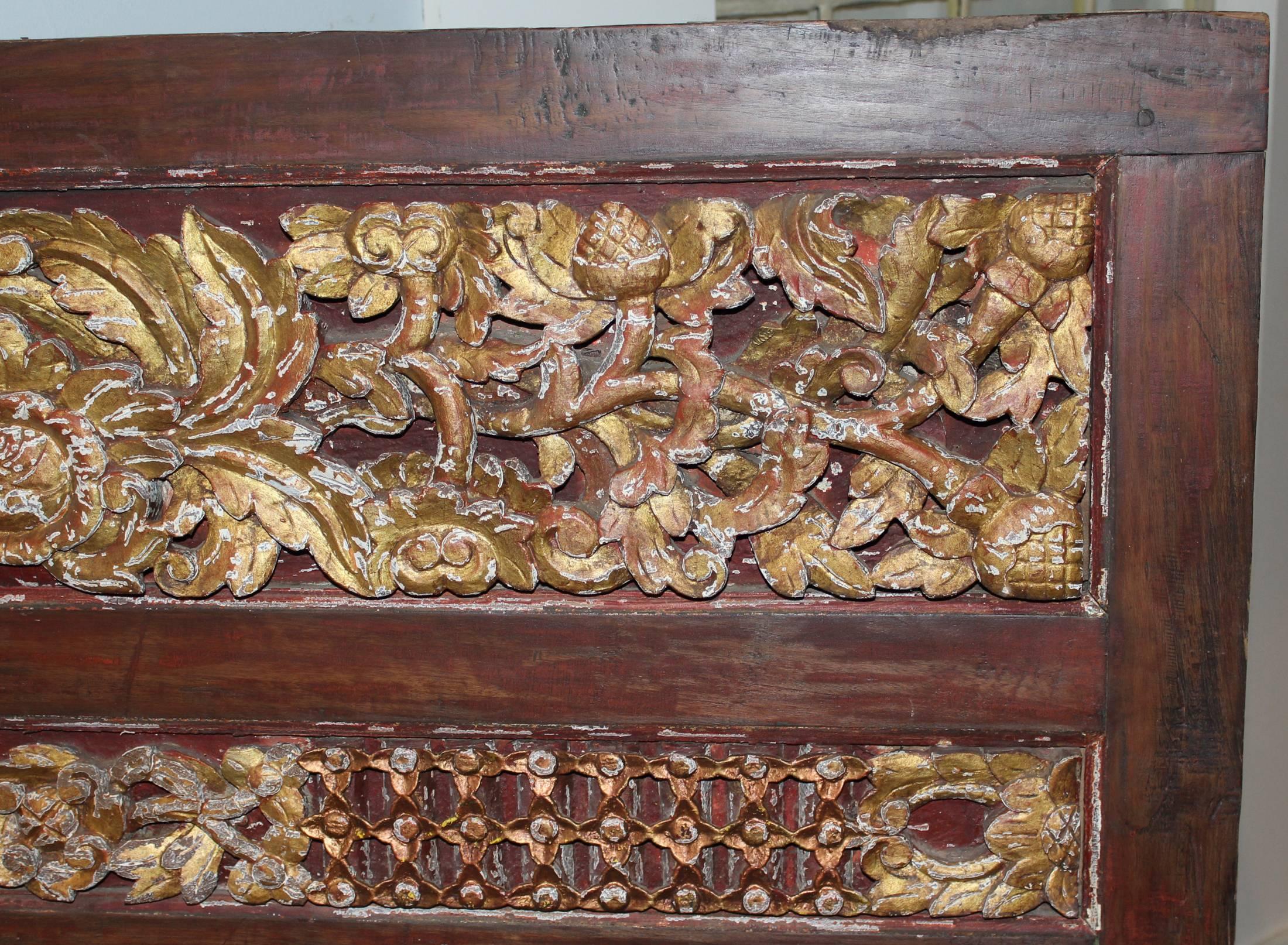 A fabulous carved Indonesian wooden panel with three large horizontal raised hand-carved panels separated by two smaller panels, each depicting a center gilt foliate crest or medallion with expanding foliate design in each direction, with a plain