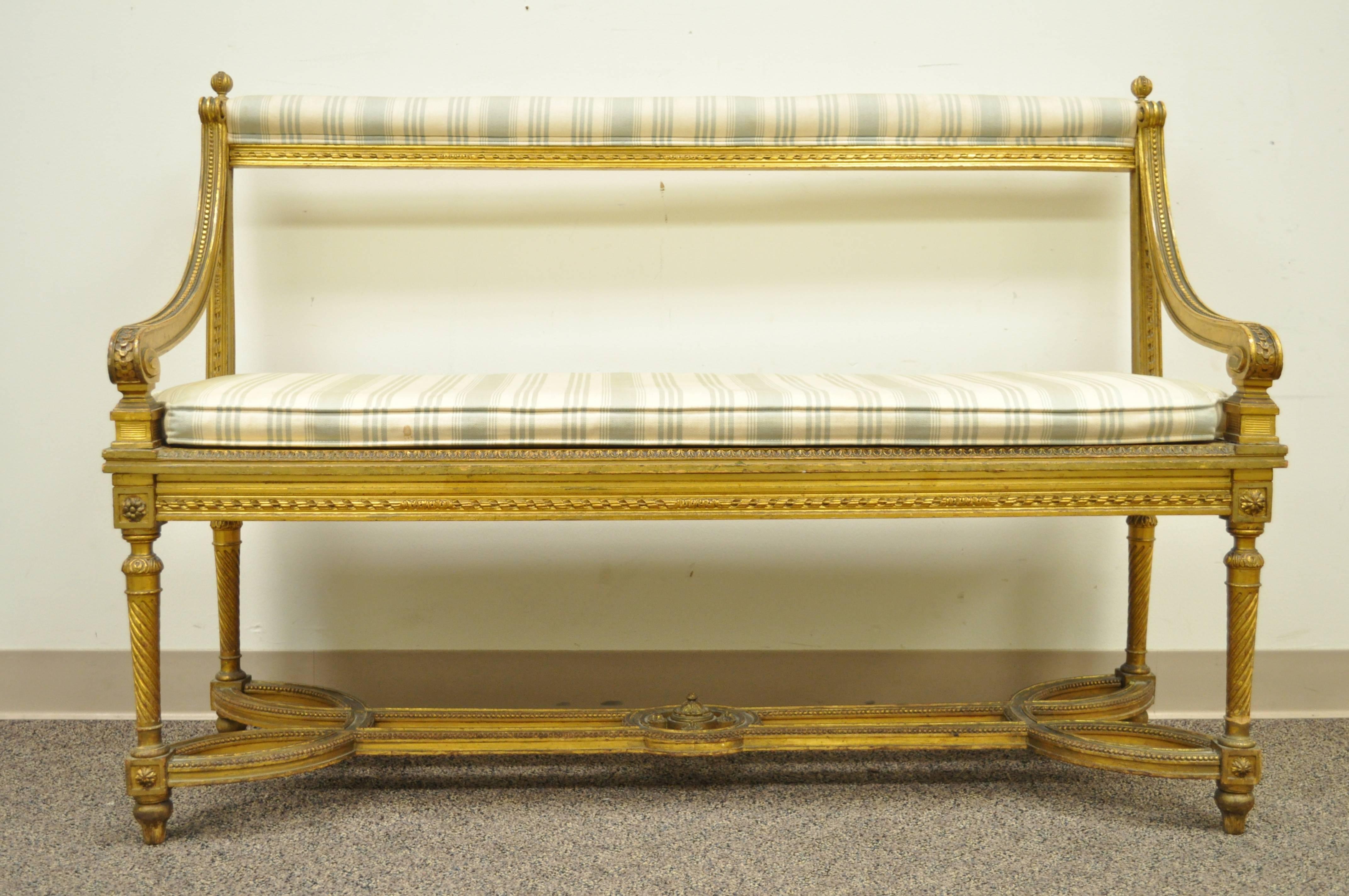 Very unique French giltwood bench in the Louis XVI taste. Item features an ornate stretcher supported base, swirl reeded legs, open back, cane seat, lose cushion, upholstered upper rail and elegant French form.

