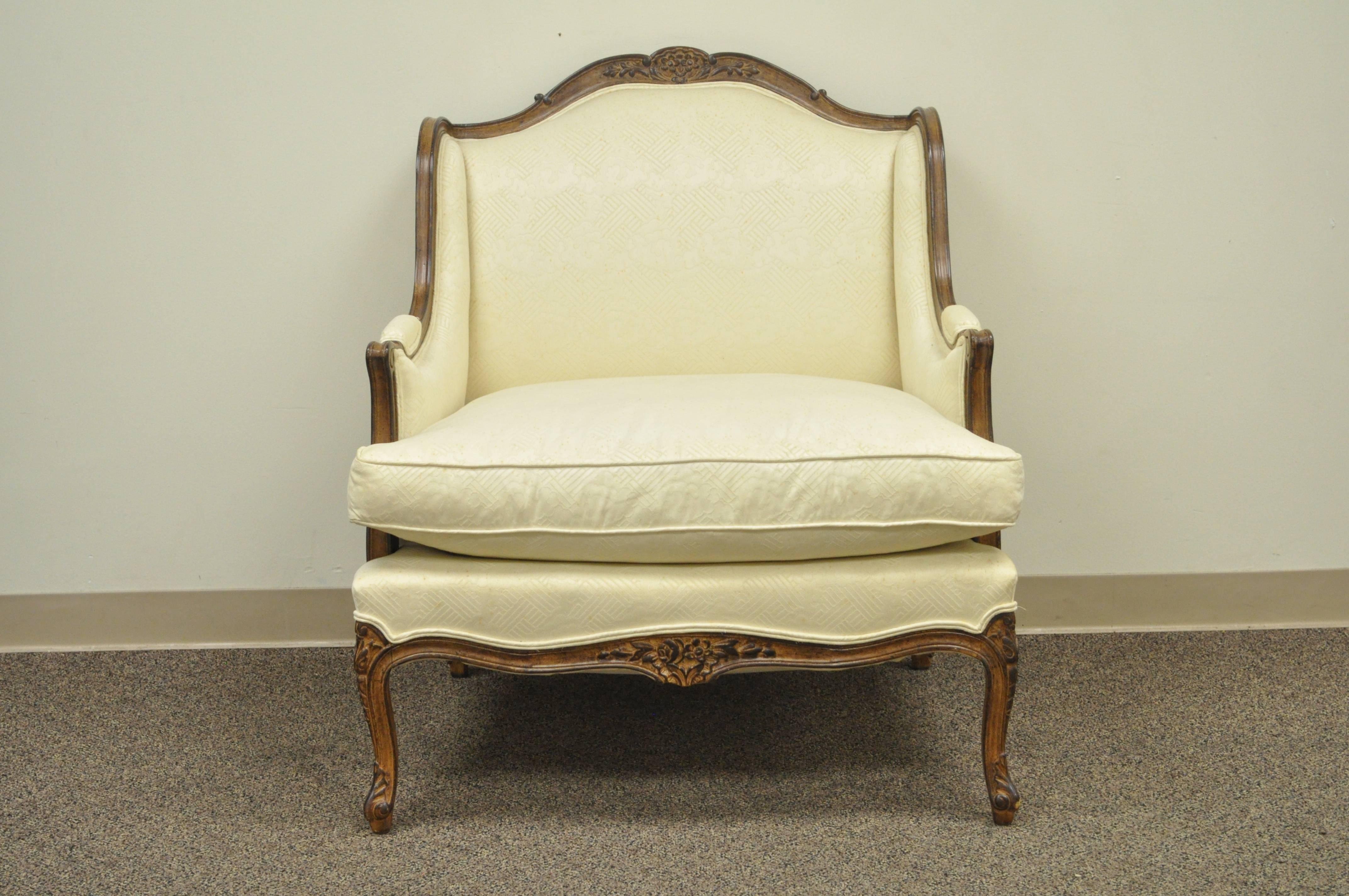 Vintage wide frame French Country / Louis XV style floral carved bergere arm chair. Lounge chair features shapely cabriole legs, floral carved accents and Classic and elegant form.
