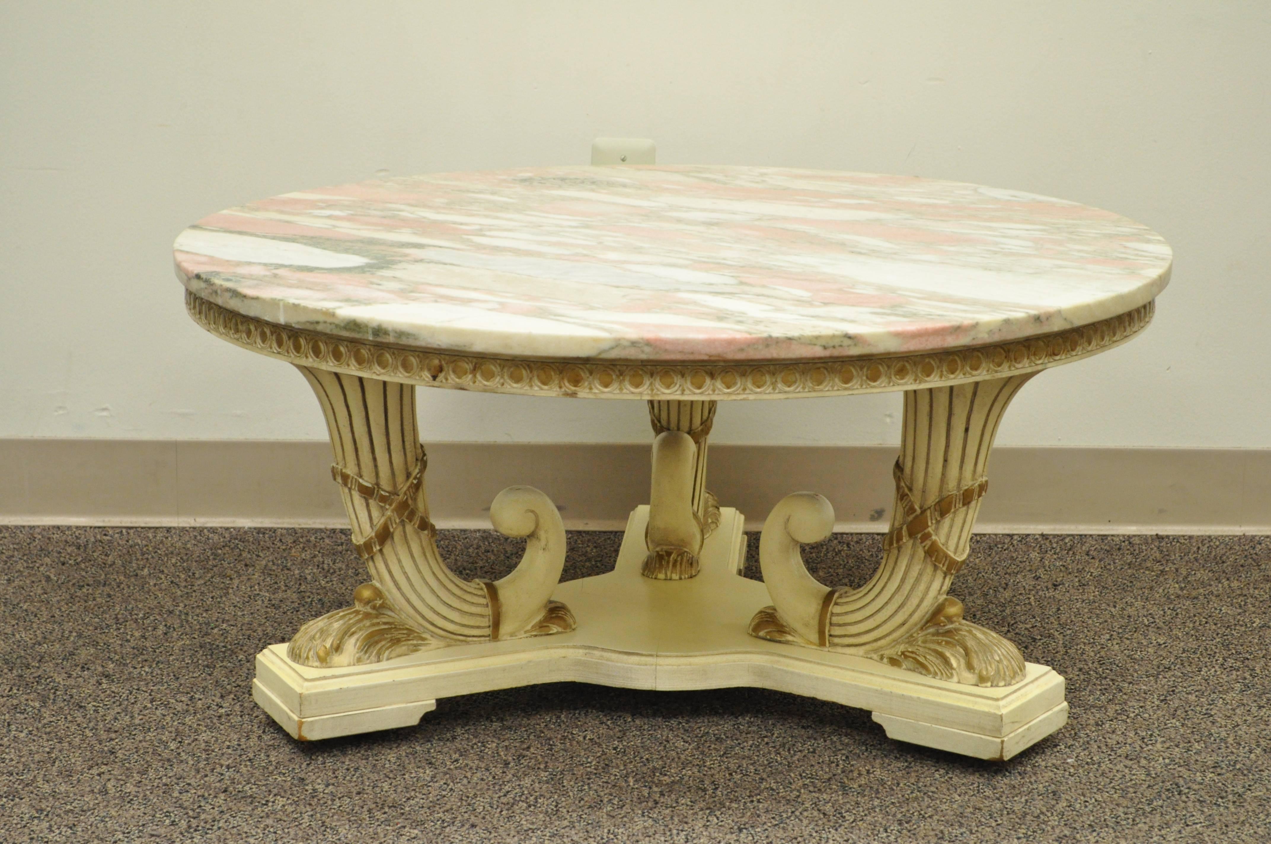 Vintage French Empire / Neoclassical style marble top coffee table. Item features a triple cornucopia carved wood base, pink round marble-top, off white original painted finish and rolling casters.