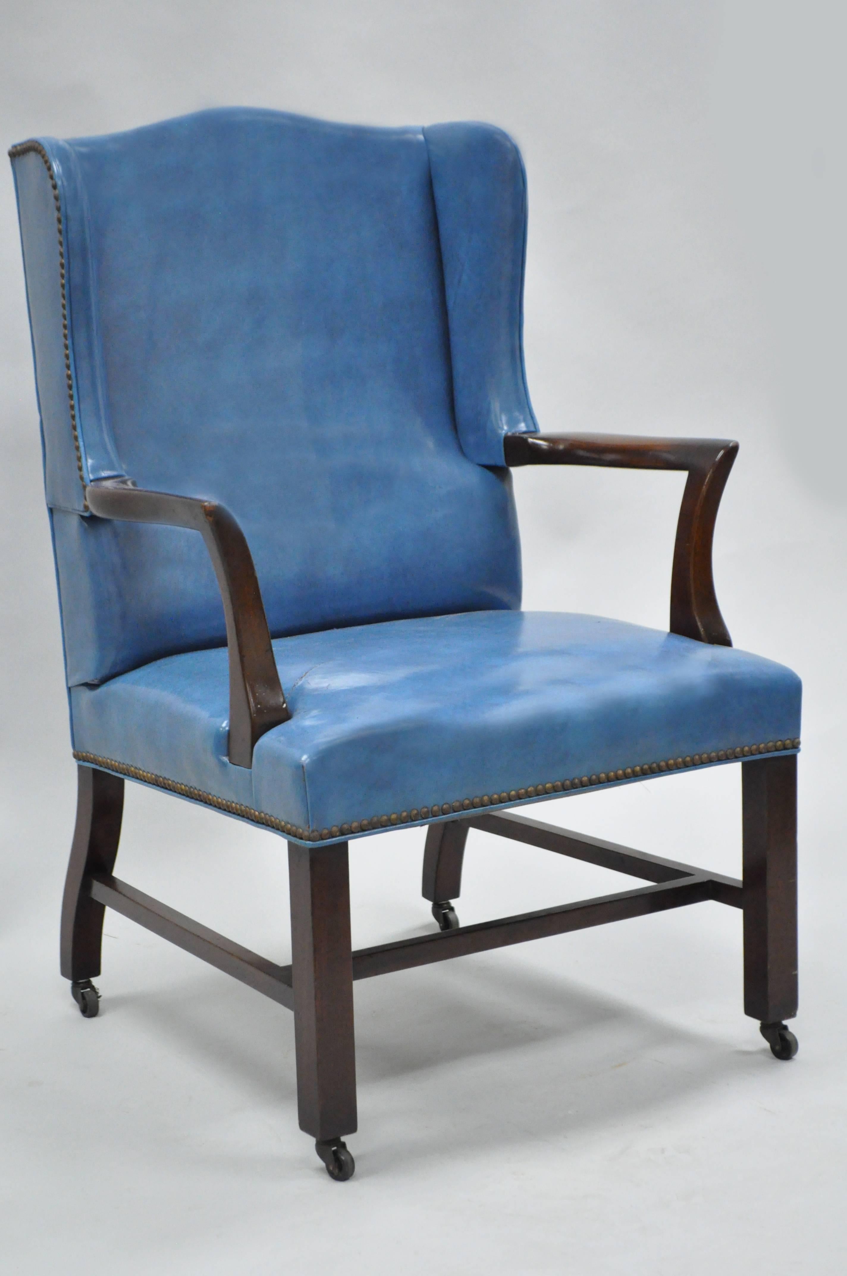 Remarkable quality mid-20th century blue leather English style library desk armchair on Casters by W&J Sloane; New York, NY in the manner of Edward Wormley. This executive chair features a heavy solid mahogany wingback frame, original blue leather