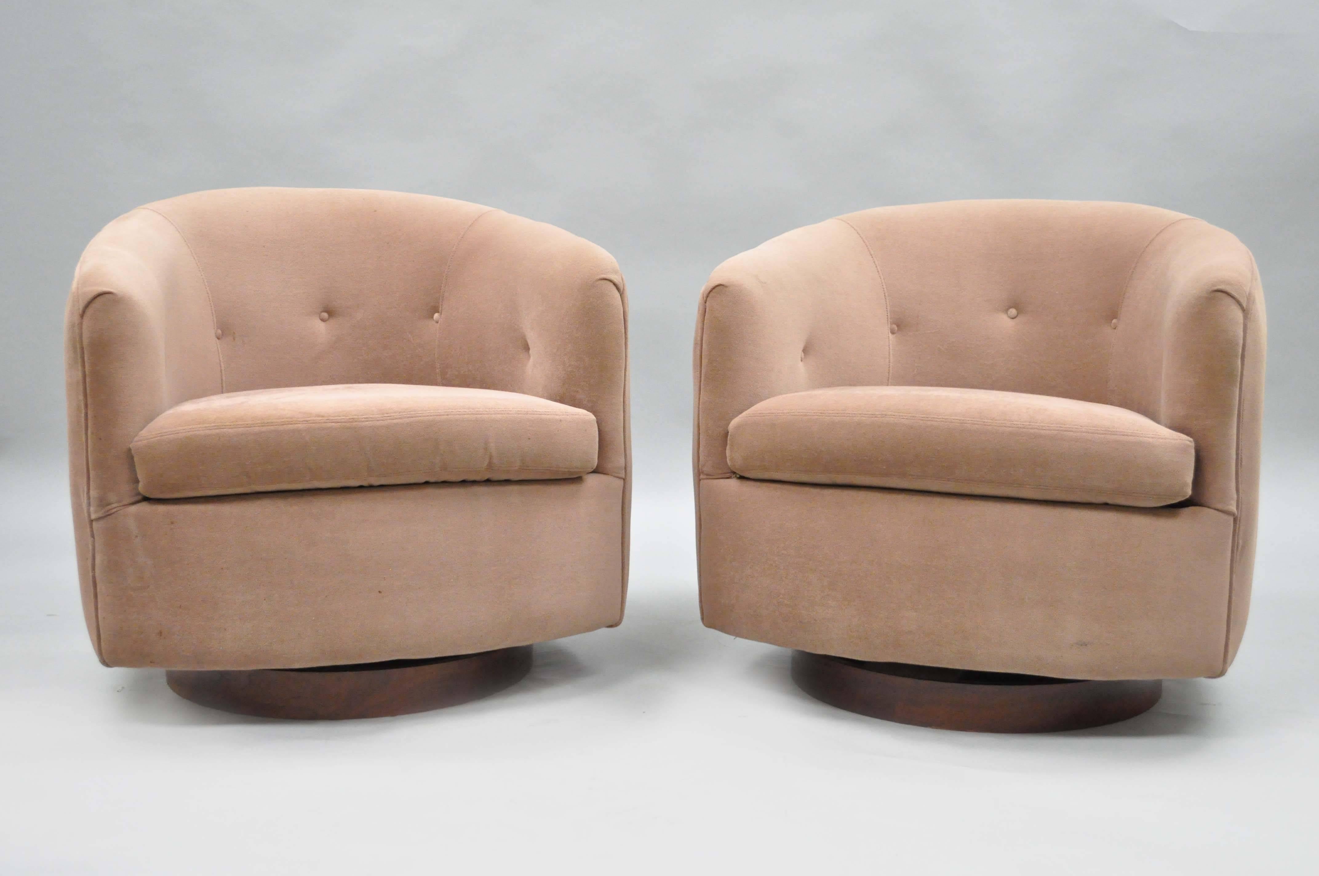 Pair of authentic Milo Baughman for Thayer Coggin swivel walnut base barrel back club chairs. This pair of Mid-Century Modern lounge chairs features rounded backs and walnut veneer swivel plinths.