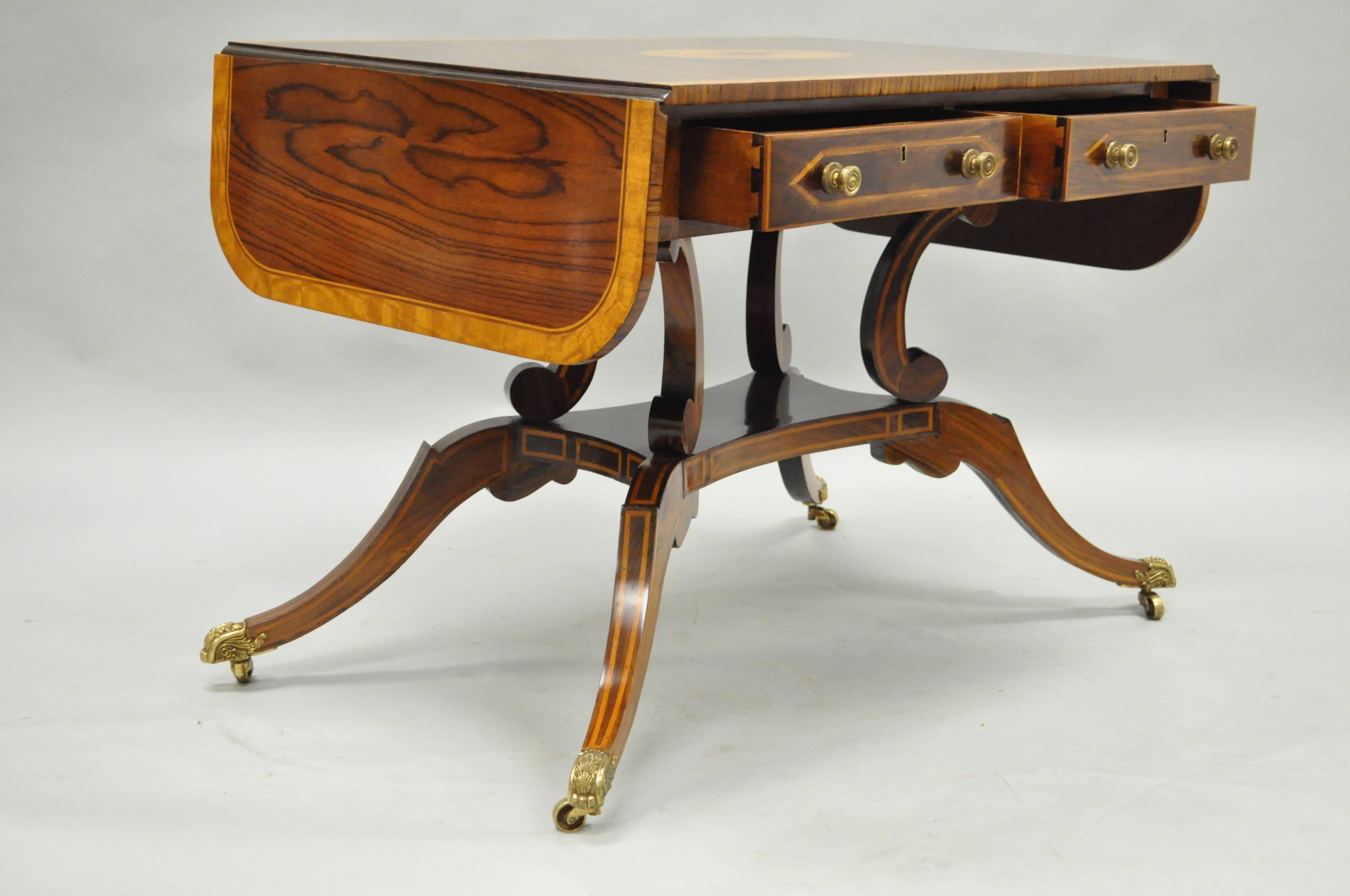 Impressive late 20th century regency/neoclassical style drop-leaf sofa table attributed to Maitland Smith. This rosewood and mahogany table features satinwood inlays and banding, pinwheel inlaid top, two dovetailed drawers, solid brass paw foot
