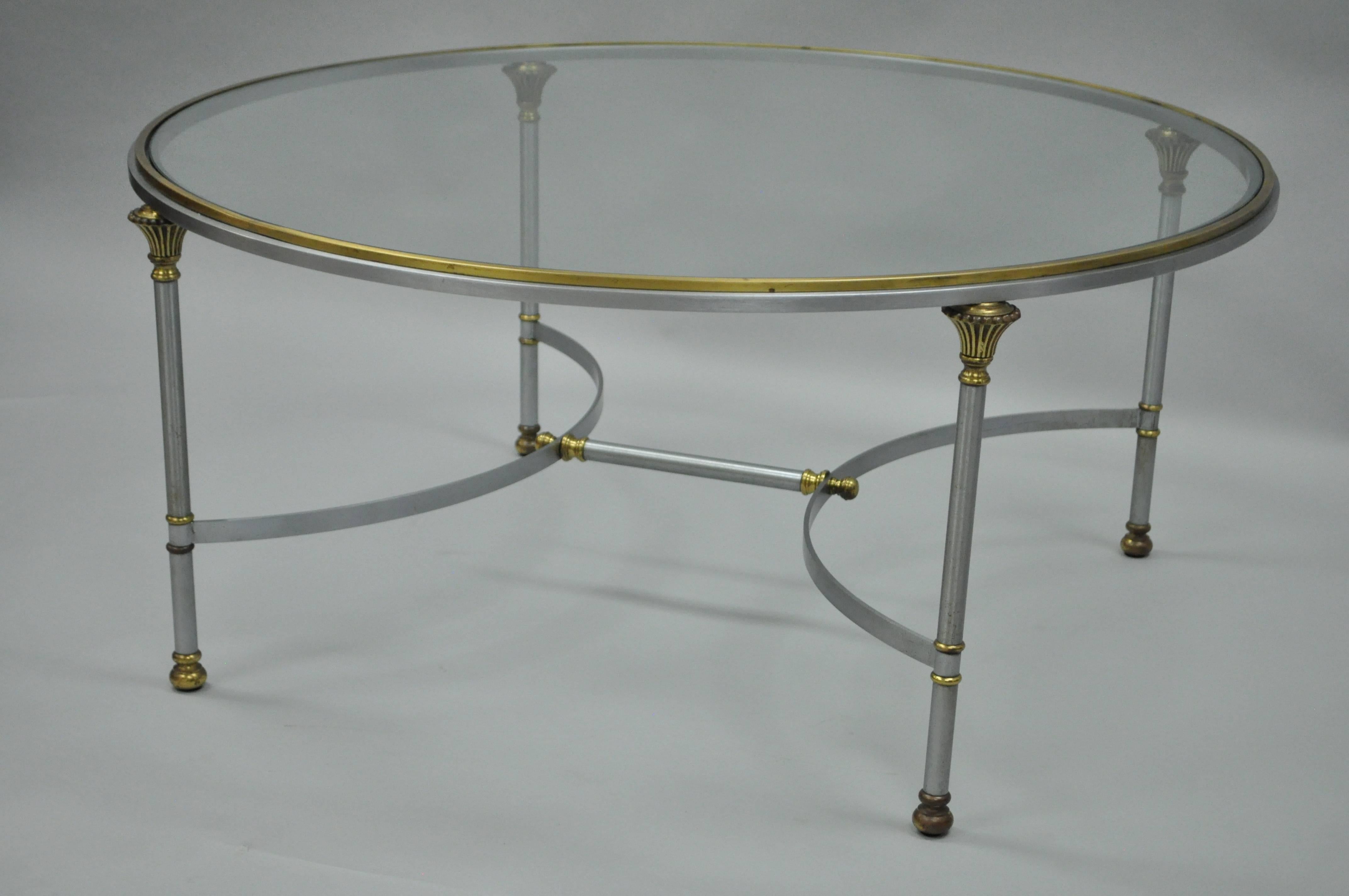 Elegant vintage Italian brushed steel and brass round cocktail table in the manner of Maison Jansen. Item features a round form with solid brass gallery, inset glass top, brushed steel stretcher supported frame, brass accents and quintessential