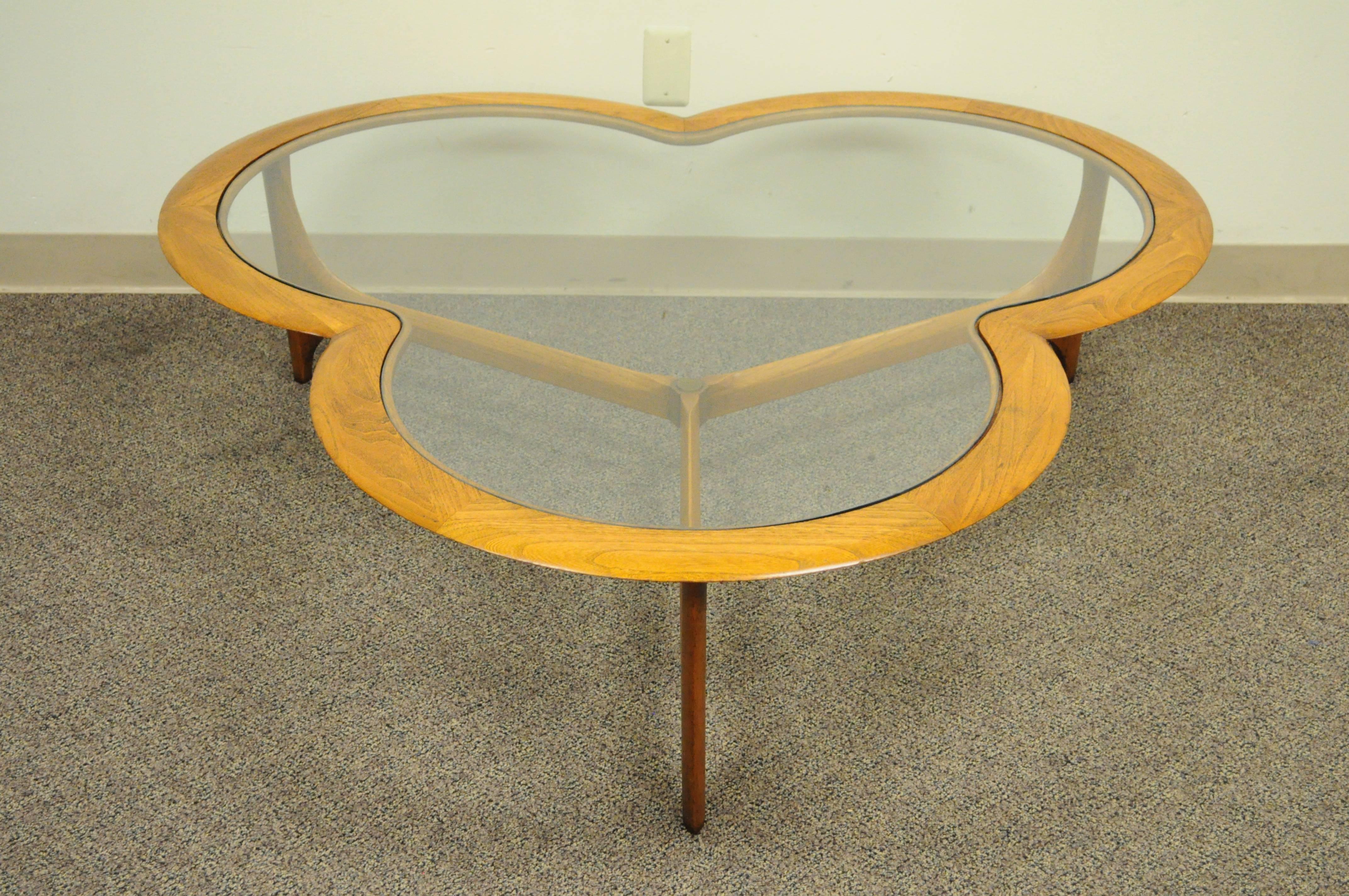 Large vintage lane three leaf clover Mid-Century Modern walnut coffee table. Item features an inset shaped glass top, sculptural three leg stretcher base with brass medallion, solid walnut frame, and great overall form.