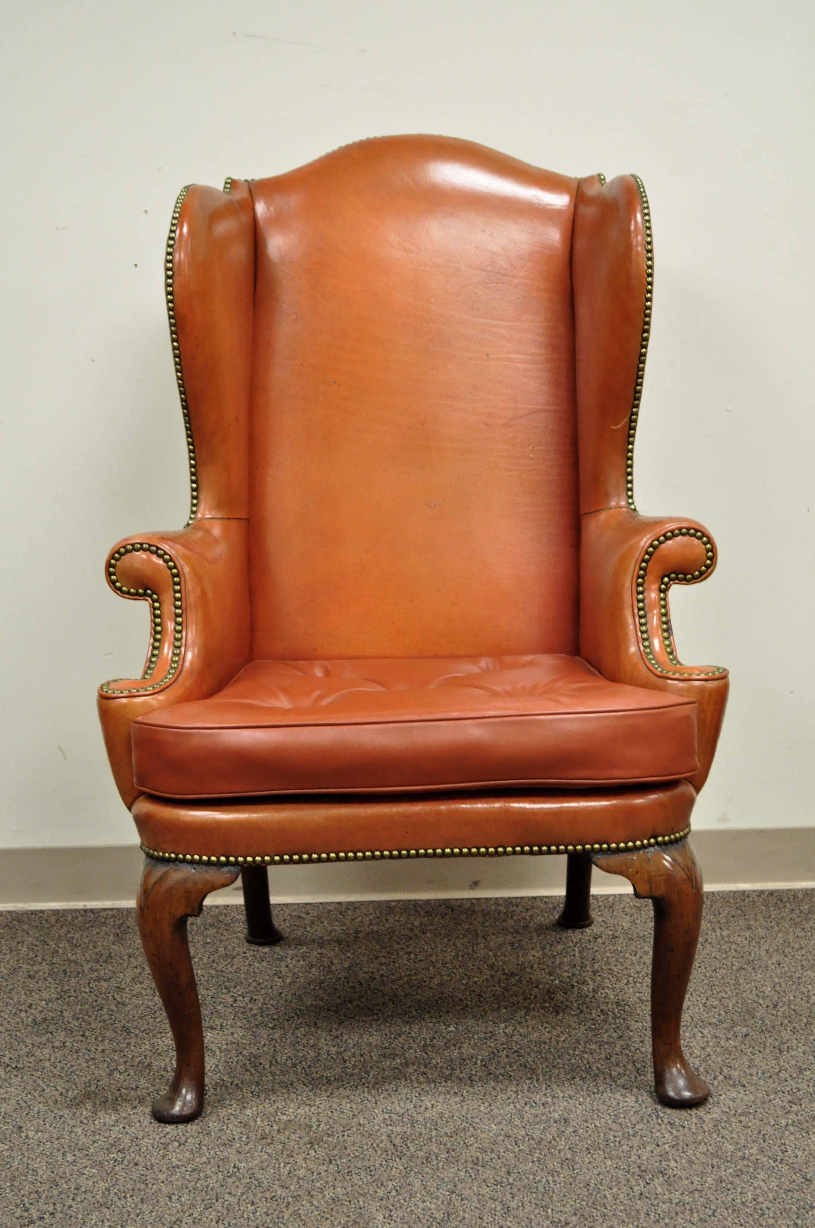 Antique 19th century burnt orange distressed leather English wingback chair. Item features a dramatic solid wood frame with rolled arms, carved Queen Anne style front legs, splayed rear legs, deep winged back, and beautiful patina to the original
