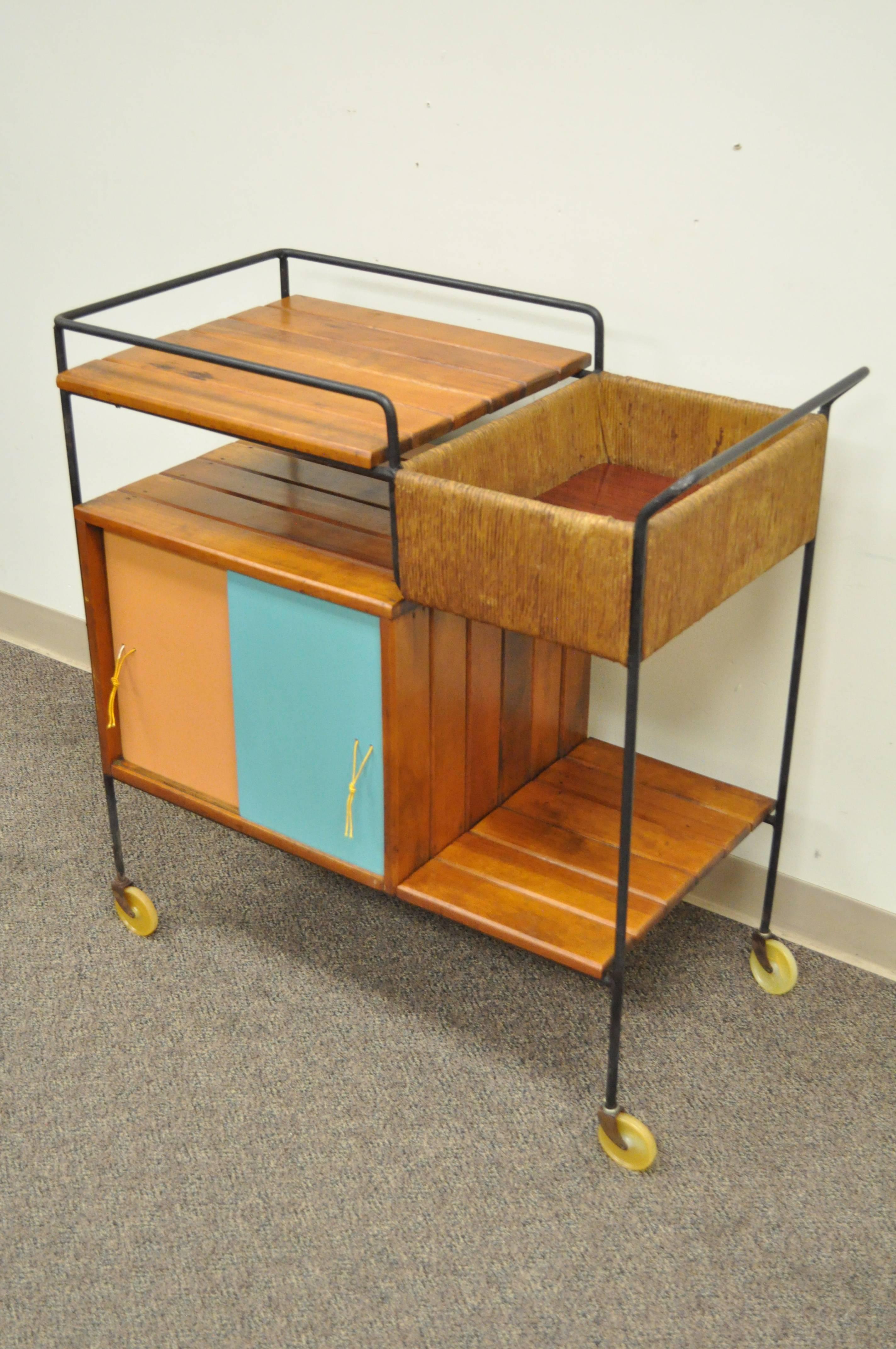 Vintage Arthur Umanoff Mid-Century Modern tiki bar cart. Item features a wrought iron frame, solid wood slatted surfaces, woven rush upper cubby and four blue and orange sliding doors with leather pulls. Great original vintage condition.