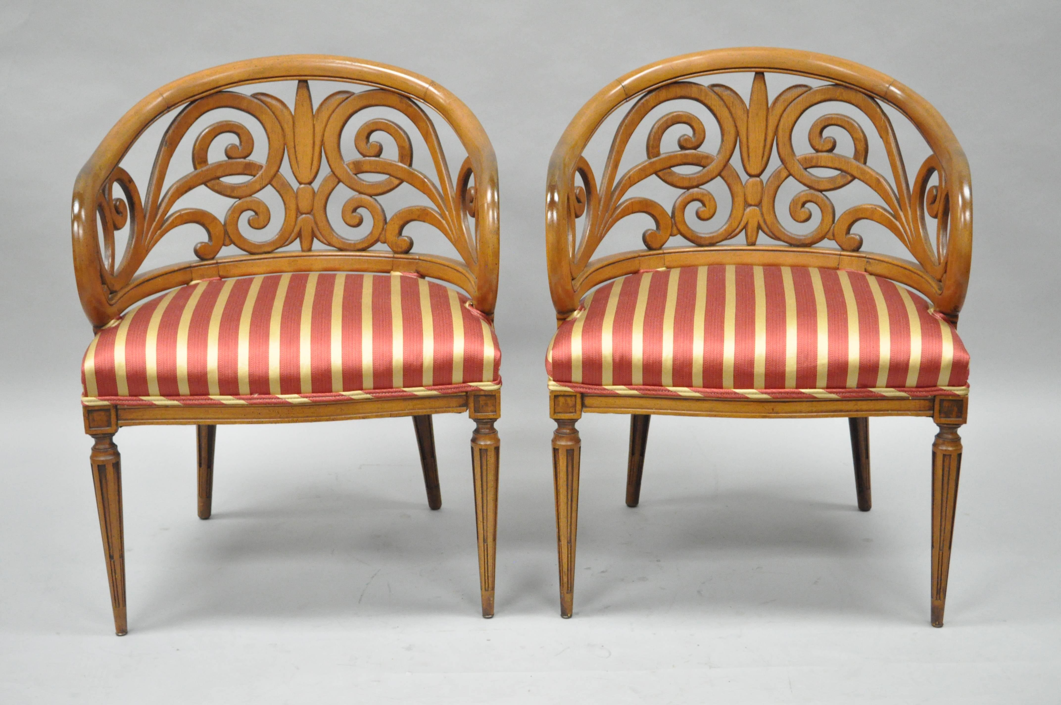 Unique pair of ornate vintage fancy barrel back Hollywood Regency chairs. Item features pierce carved whimsical barrel back walnut frames with bell flower central design, reeded and tapered legs, and great French Hollywood Regency form. Style very
