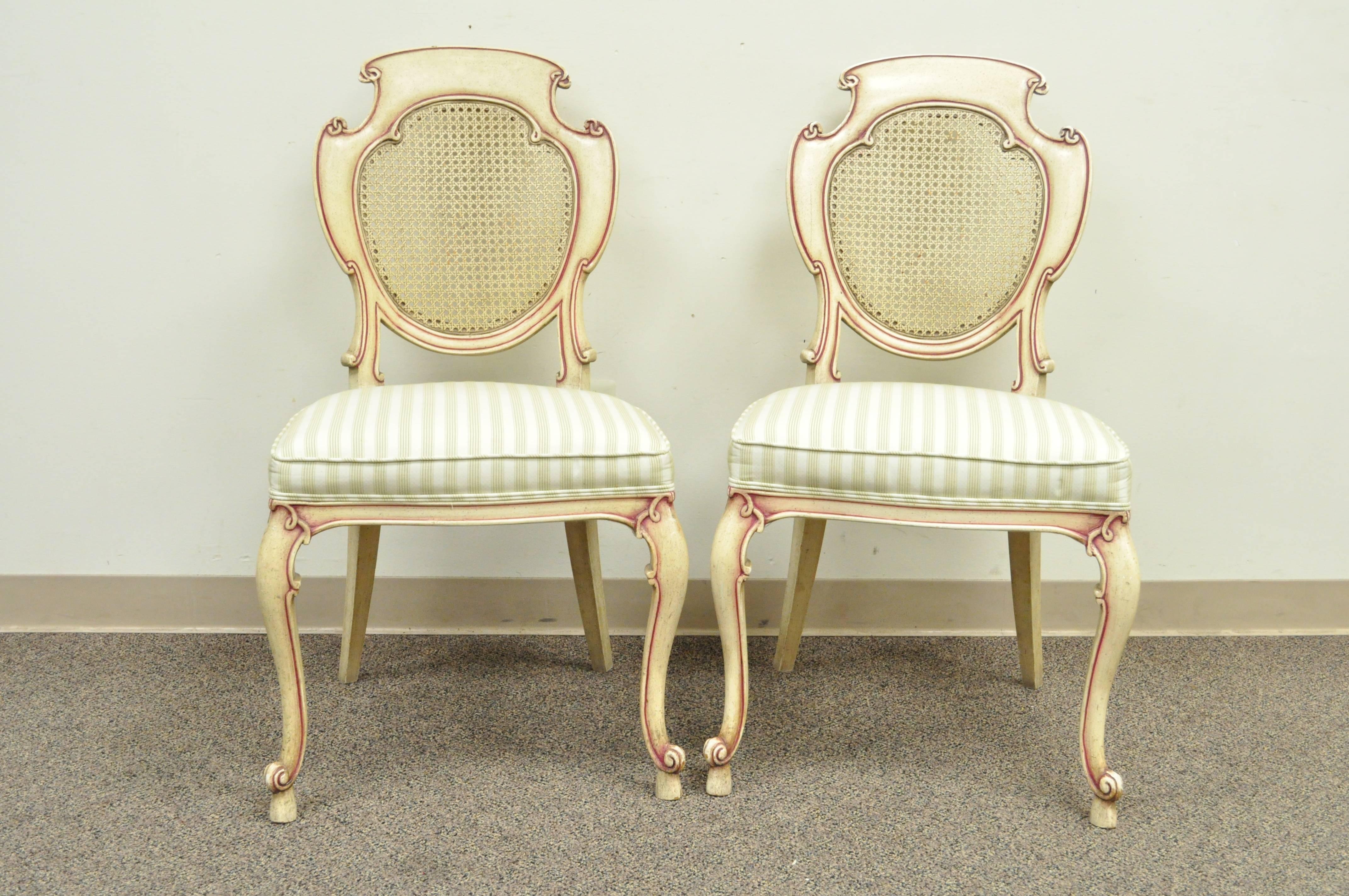 Very unique set of four vintage scroll carved Italian Hollywood Regency cream and pink painted side chairs. Chairs feature carved solid wood frames, caned backs, cabriole legs in the French style, and upholstered seats. Each back is scroll carved
