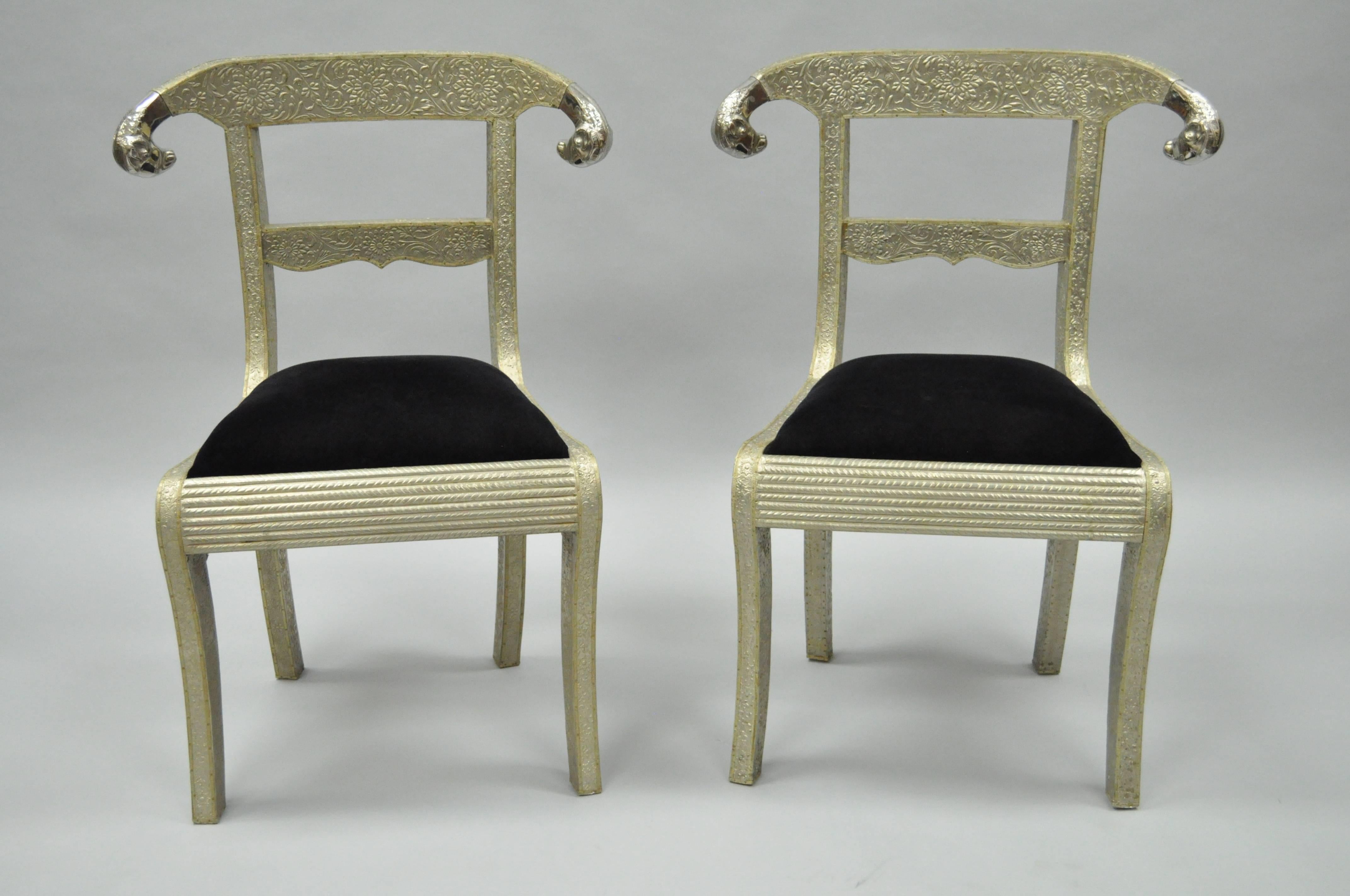 Desirable pair of vintage Anglo-Indian dowry side chairs with ram's head accents. These wonderful chairs feature wooden frames clad in floral embossed silver metal and polished scrolling rams heads. Seats are upholstered in a black velvet fabric.