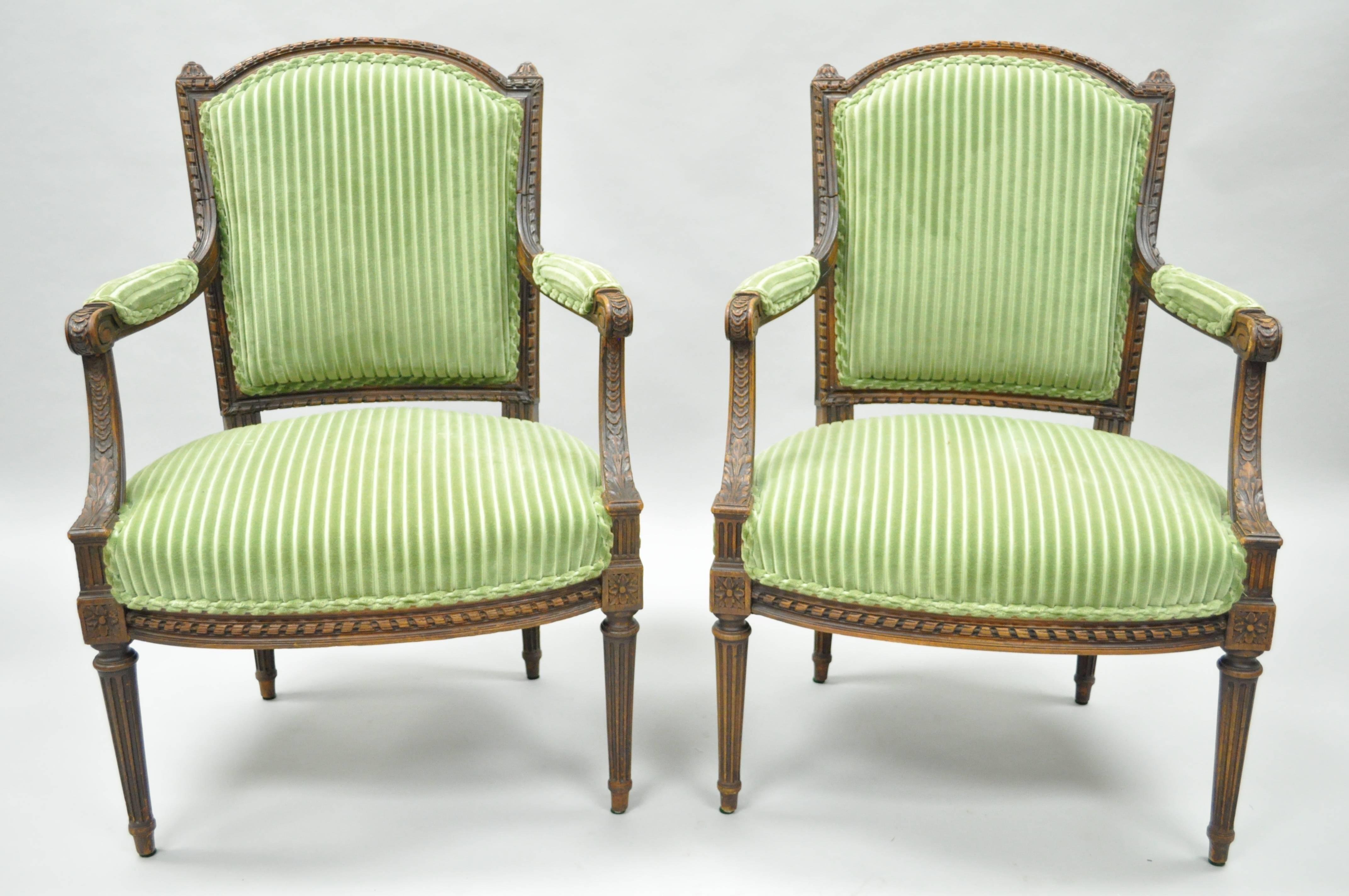 Remarkable pair of early 20th century French Louix XVI/Directoire style carved walnut armchairs. Chairs feature finely carved solid walnut wood frames, reeded and tapered legs, green upholstered frames, padded armrests and elegant French form.