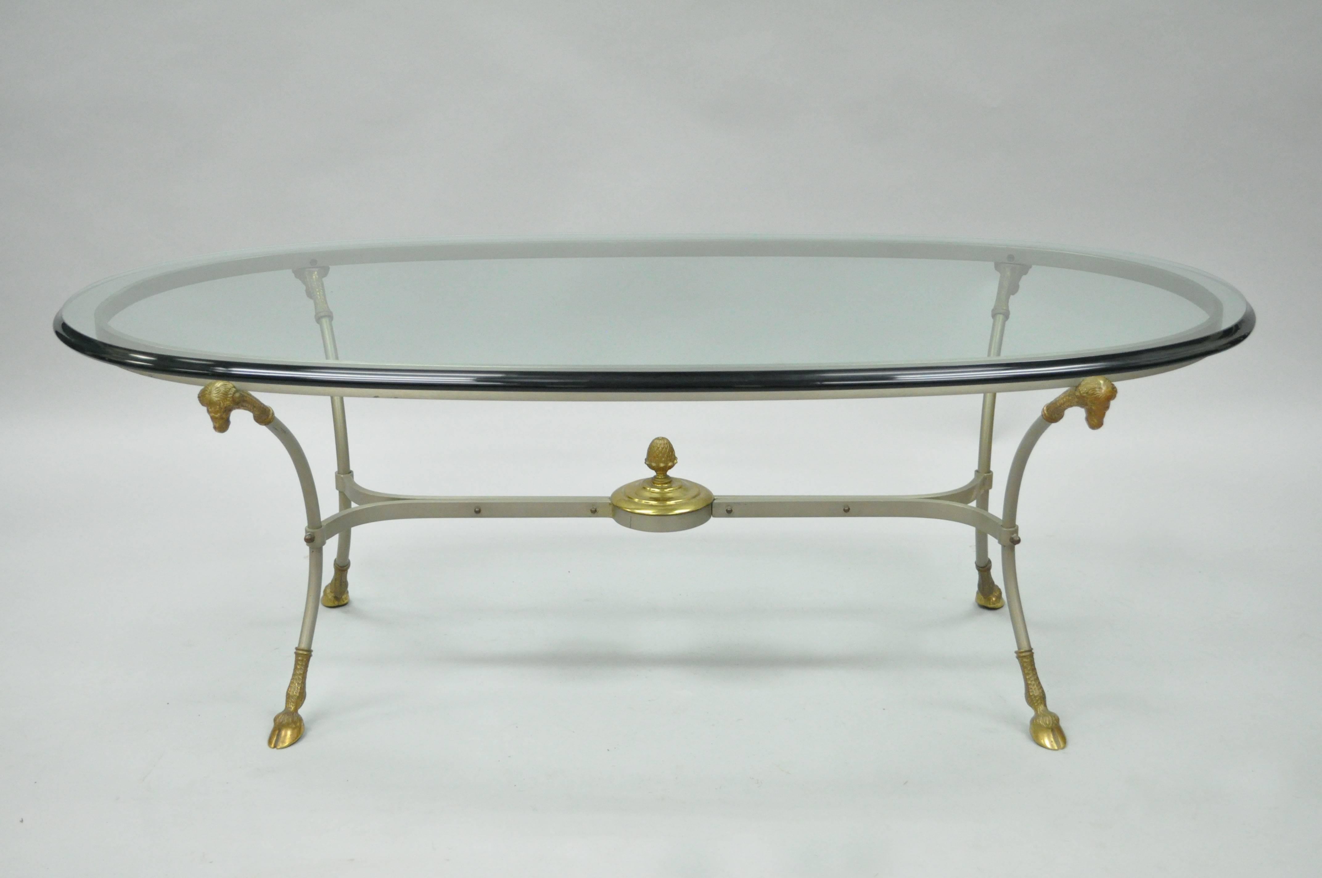 Quality vintage Italian brass and steel Regency style oval coffee table. Item features a thick oval beveled glass top, steel frame with brass ram / goat heads, hairy hoof feet, and central acorn finial. Very rare to find this model coffee table.