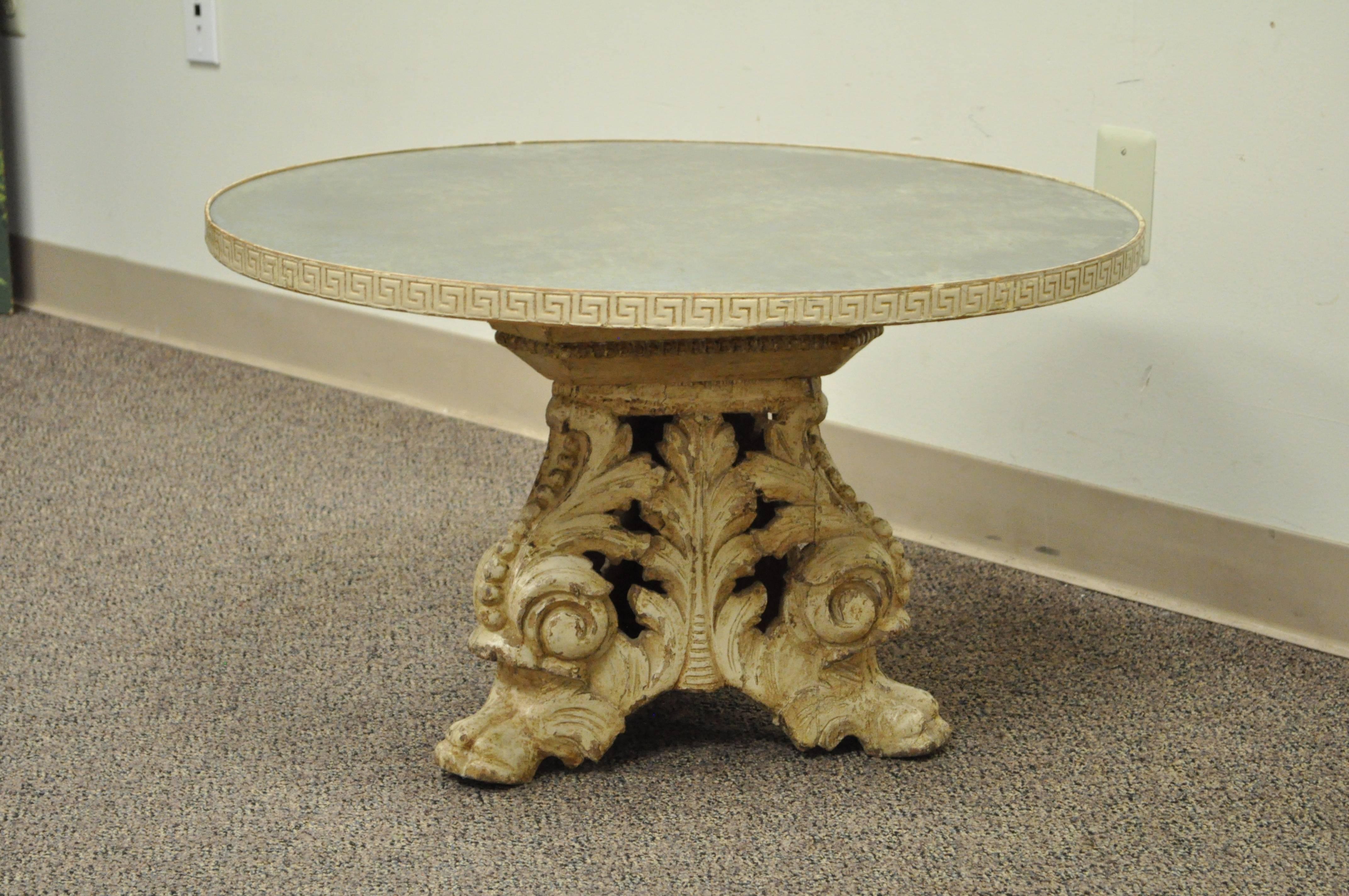 Antique Italian Baroque style round coffee table. Item features an églomisé distressed glass top, carved Greek key banding, solid hand-carved wood acanthus and paw foot pedestal base, and a desirable cream distress painted finish. The base is