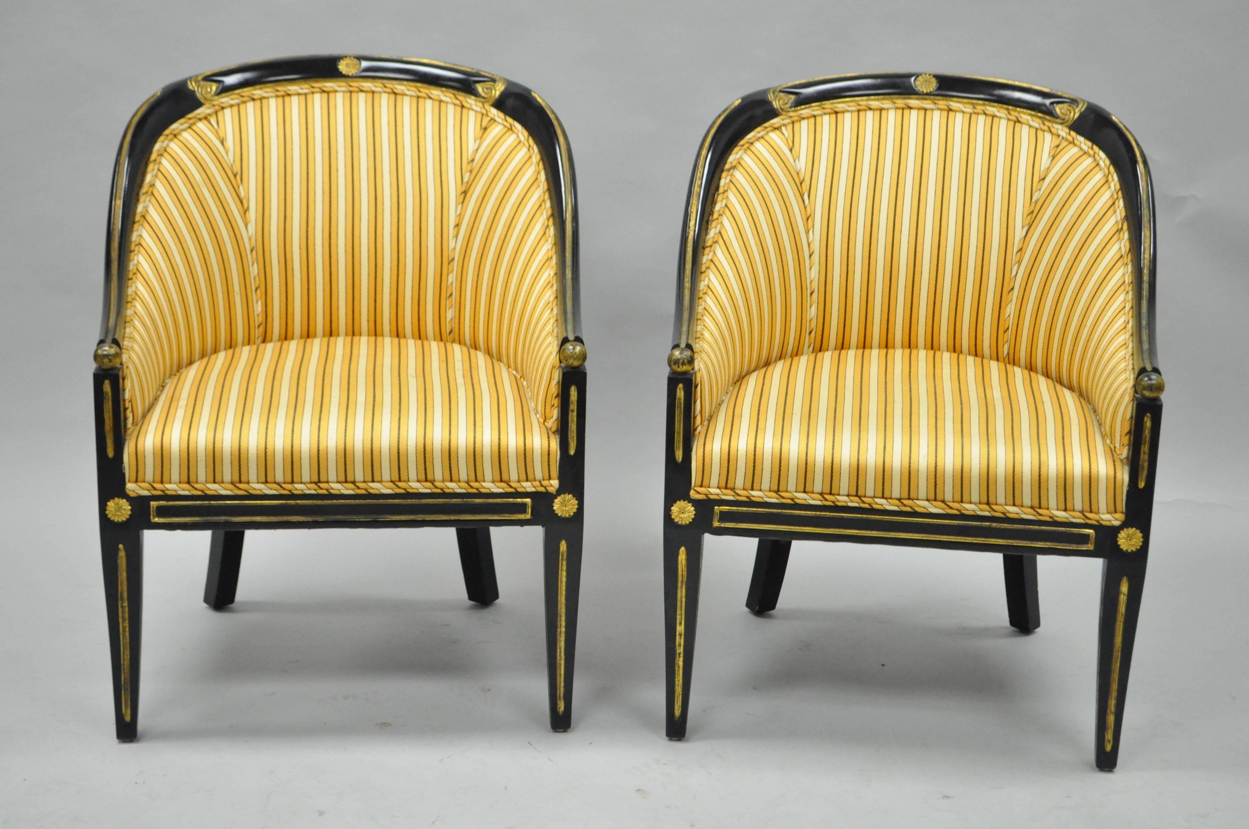 Pair of vintage black ebonized and gold neoclassical / Regency style barrel back accent chairs. This item features black lacquered solid wood barrel back frames, antiqued gold painted accents and trim, striped gold fabric, saber / Klismos legs, very