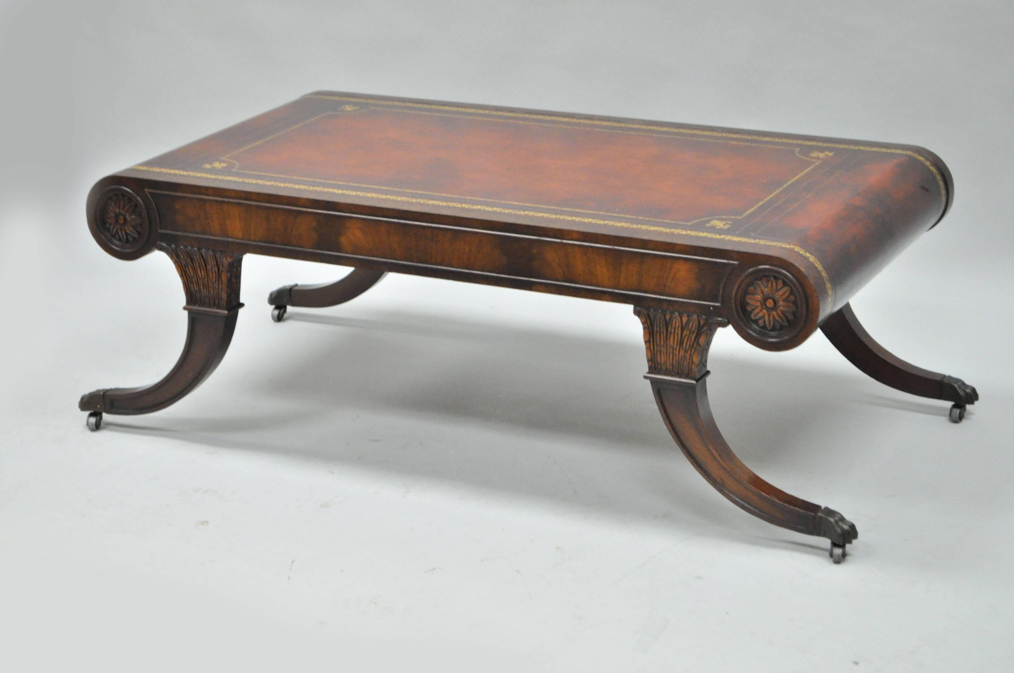 Rare vintage Regency style tooled leather and crotch mahogany coffee table by Weiman. Item features a rolled edge burgundy tooled leather top with gold gilt detailing, saber legs raised on rolling casters and brass claw feet, figured crotch mahogany