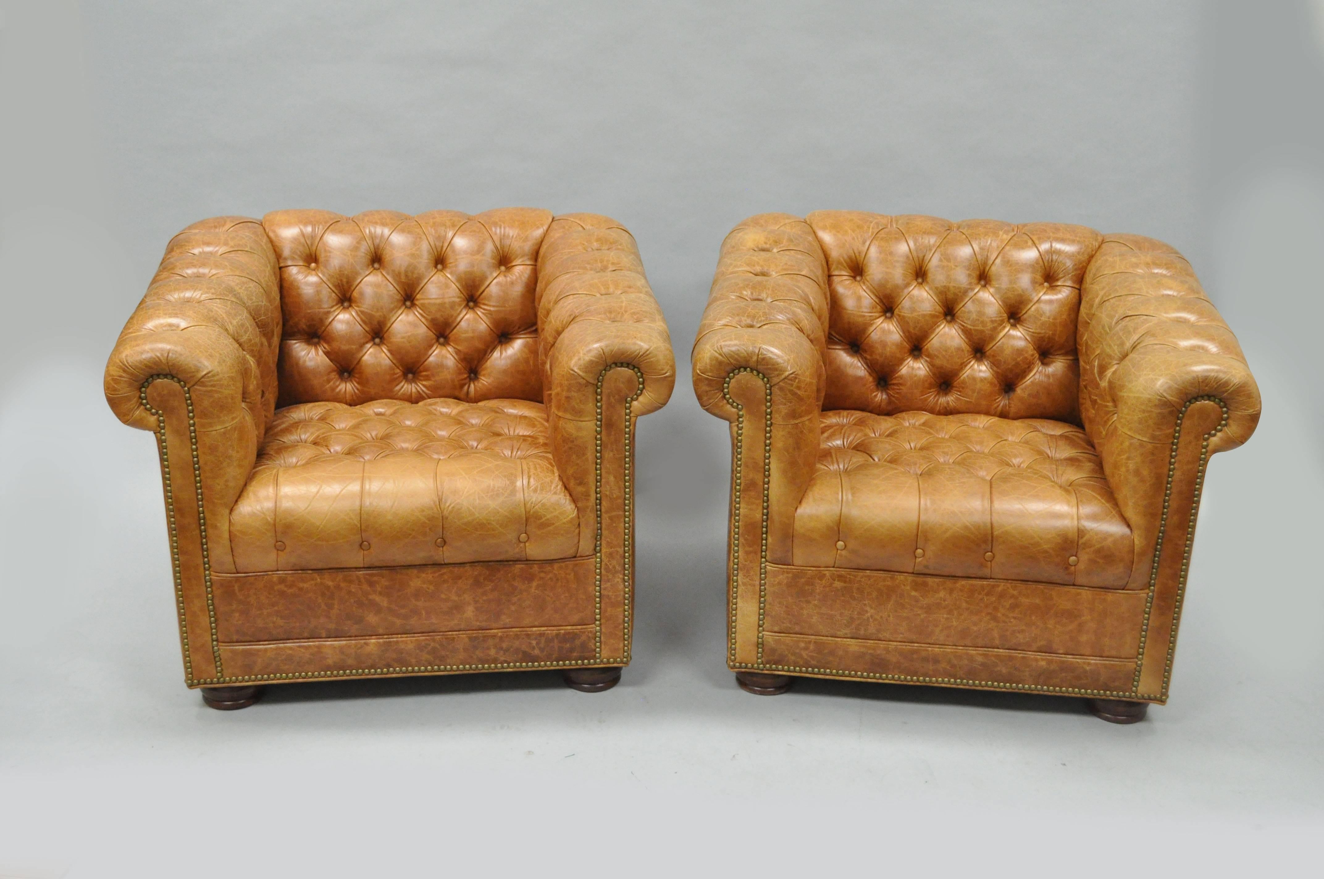 Quality pair of 21st century button tufted Chesterfield style distressed cognac leather churchill lounge or club chairs by Leathercraft. Chairs feature deep button tufted distressed leather upholstery, nailhead trim, solid maple wood bun feet on the