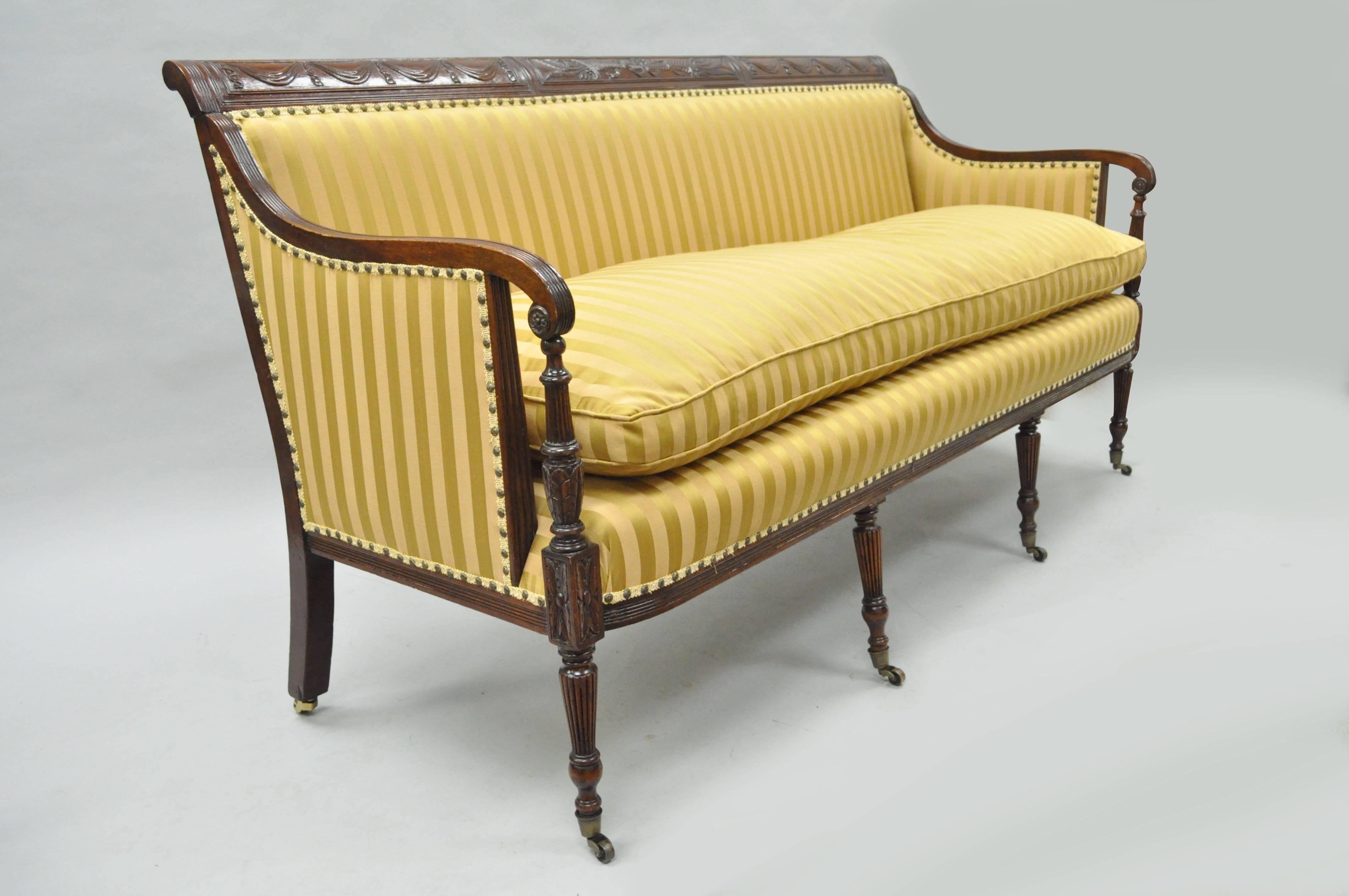 Antique American Federal carved mahogany Sheraton style sofa believed to be circa mid-late 1800s. Item features a finely carved solid mahogany frame, drape carved back rail with feather and corucopia central carving, rolling casters, gold striped