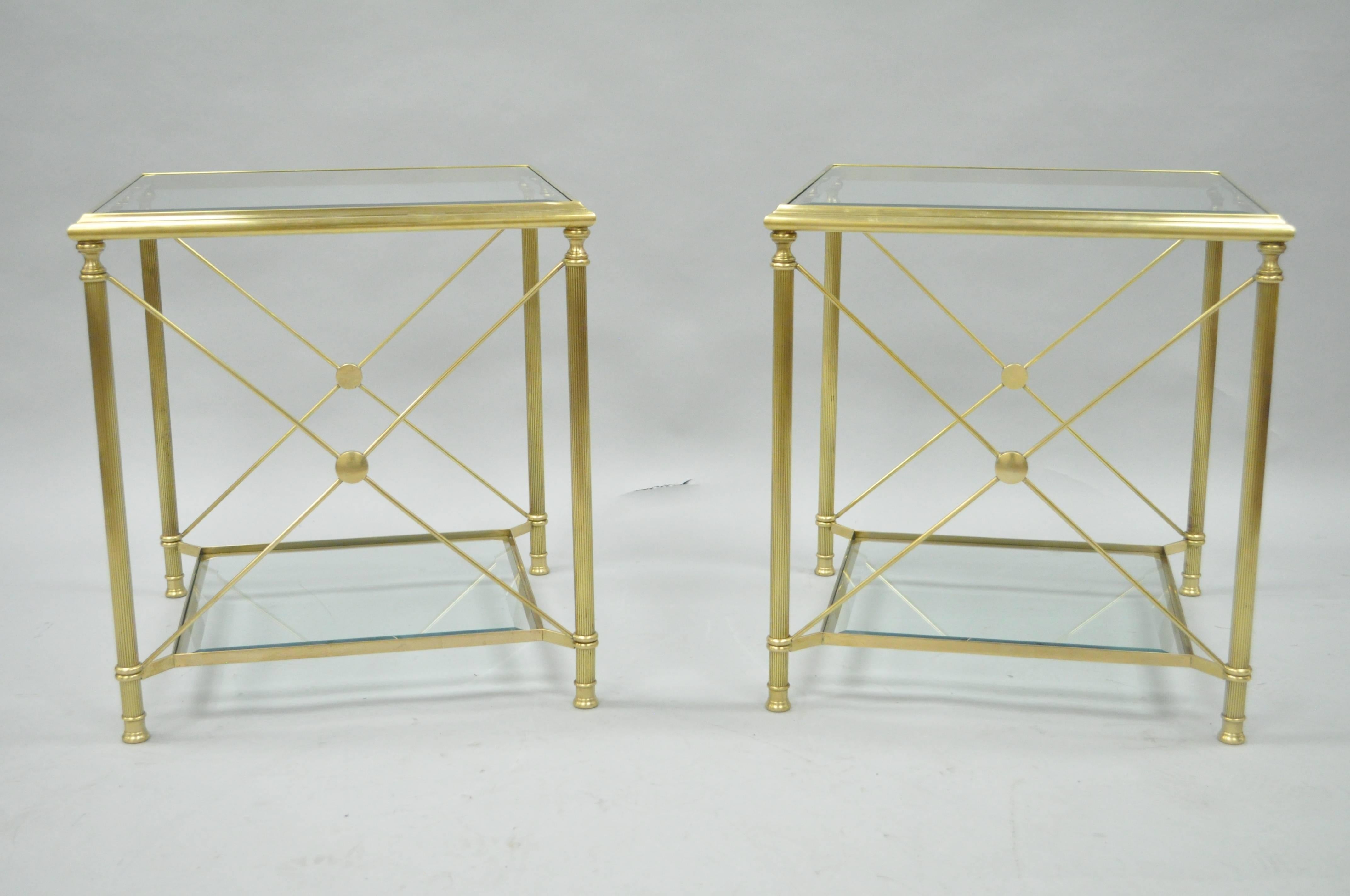 Quality pair of two-tier brass and glass neoclassical style X-form Mid-Century square side tables. Tables feature two-tier brass frames with inset beveled glass, two X-form sides and two open sides, reeded column-form legs, lower tier with extended