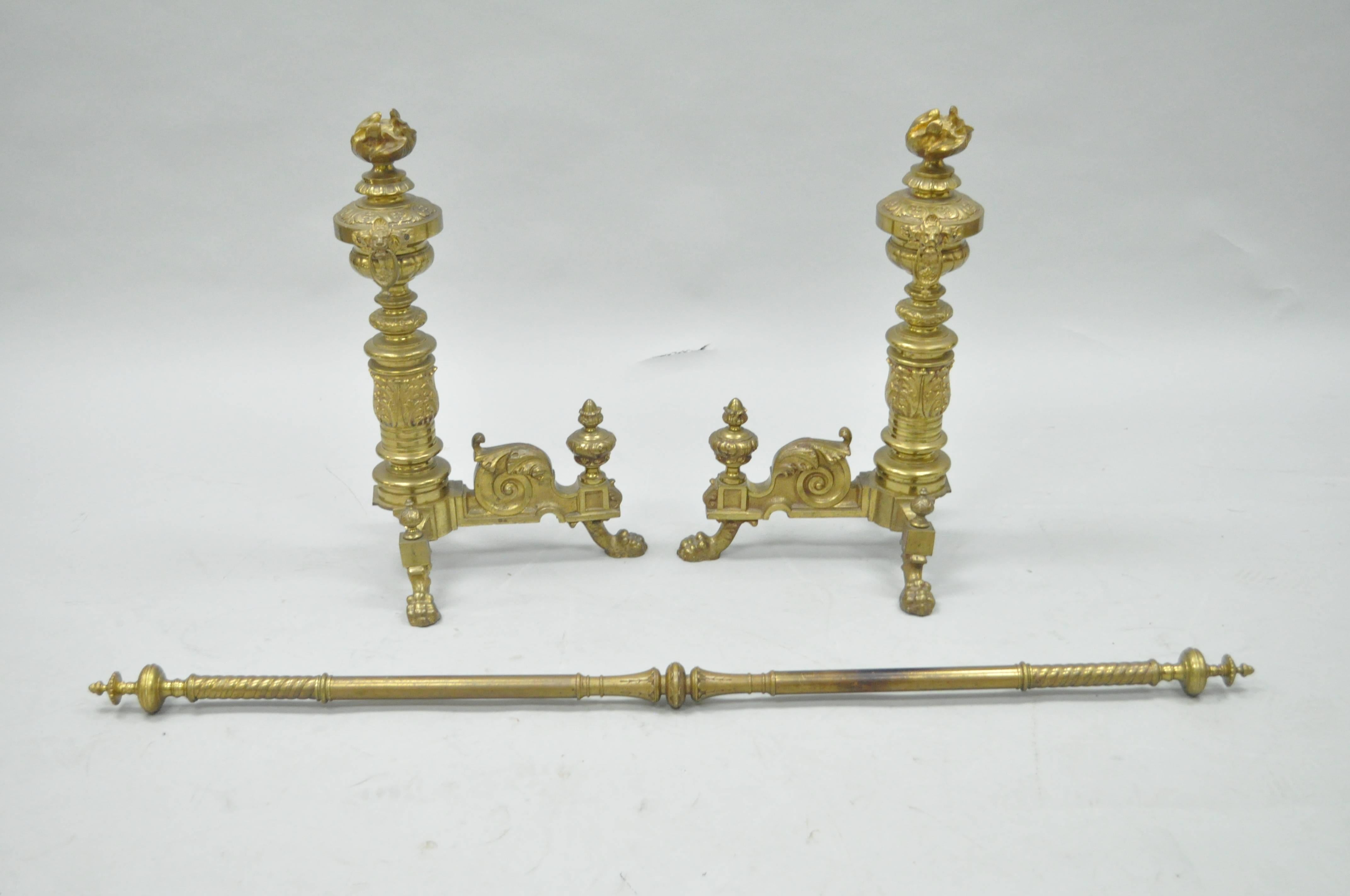Remarkable Pair of 19th Century French Neoclassical Flame & Lion Brass Paw Foot Andirons with Bar. Set features an ornate pair of cast brass andirons with flame finials, mounted with lion heads and drop rings, acanthus details, paw feet, and ornate