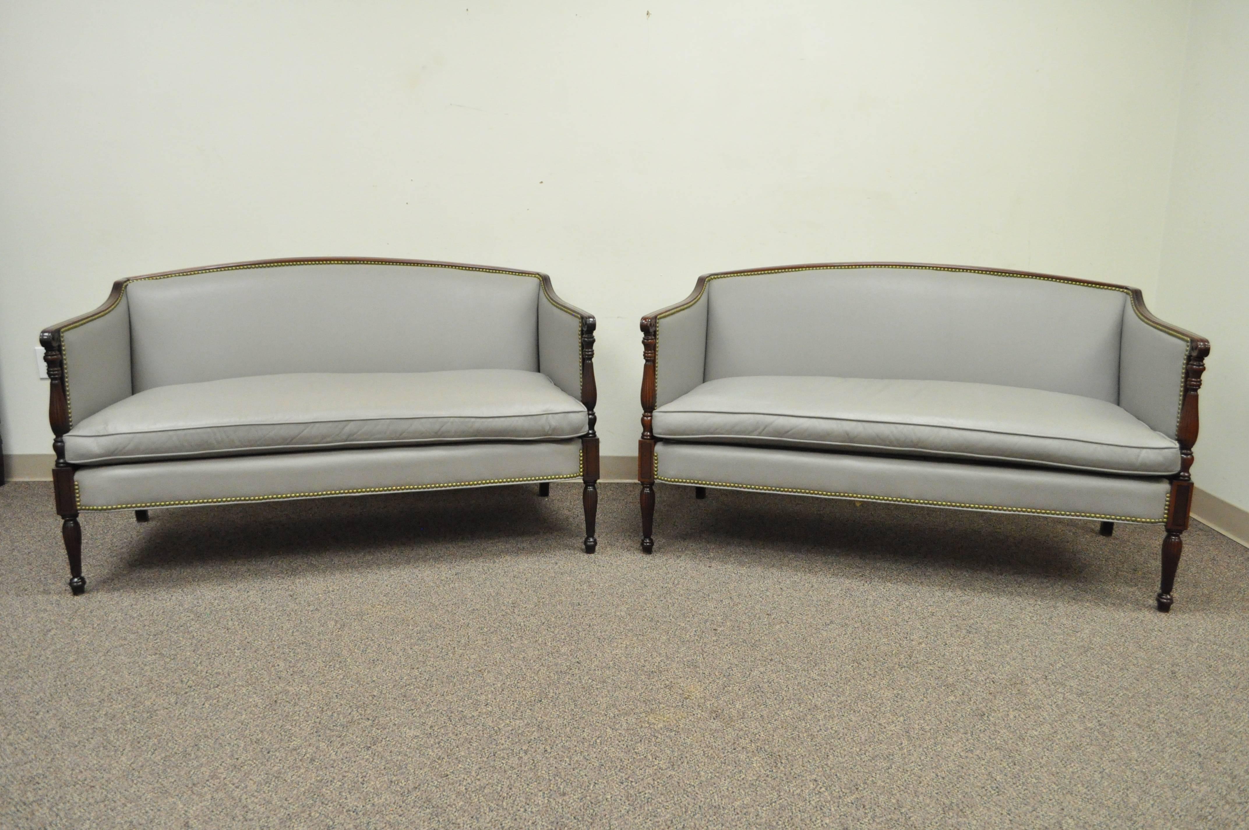 Pair of mahogany and grey leather vintage loveseats by Old Hickory Tannery. Item features original grey leather upholstery, carved solid mahogany frames, brass nailhead trim. Made in America. Measurements: 33.5