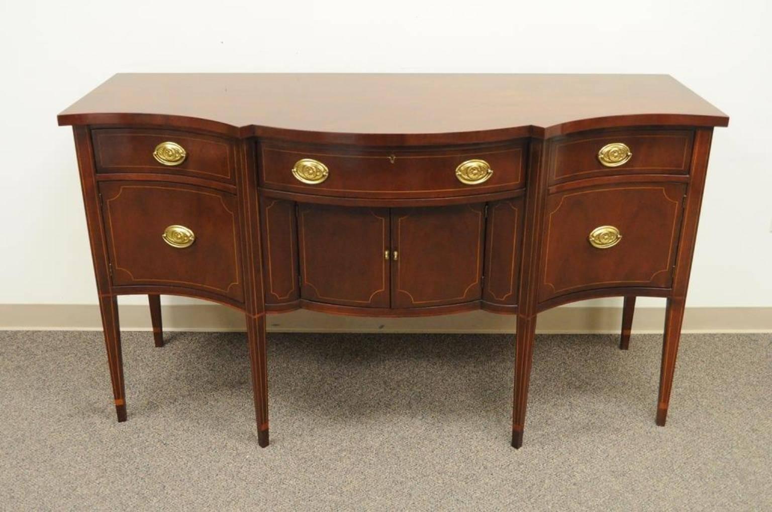 Vintage Baker Furniture Co. inlaid mahogany bow front sideboard. Item features four drawers, three lower swing door sections, beautiful satinwood inlays, polished brass hardware, tapered inlay detailed legs, elegant and classy high quality