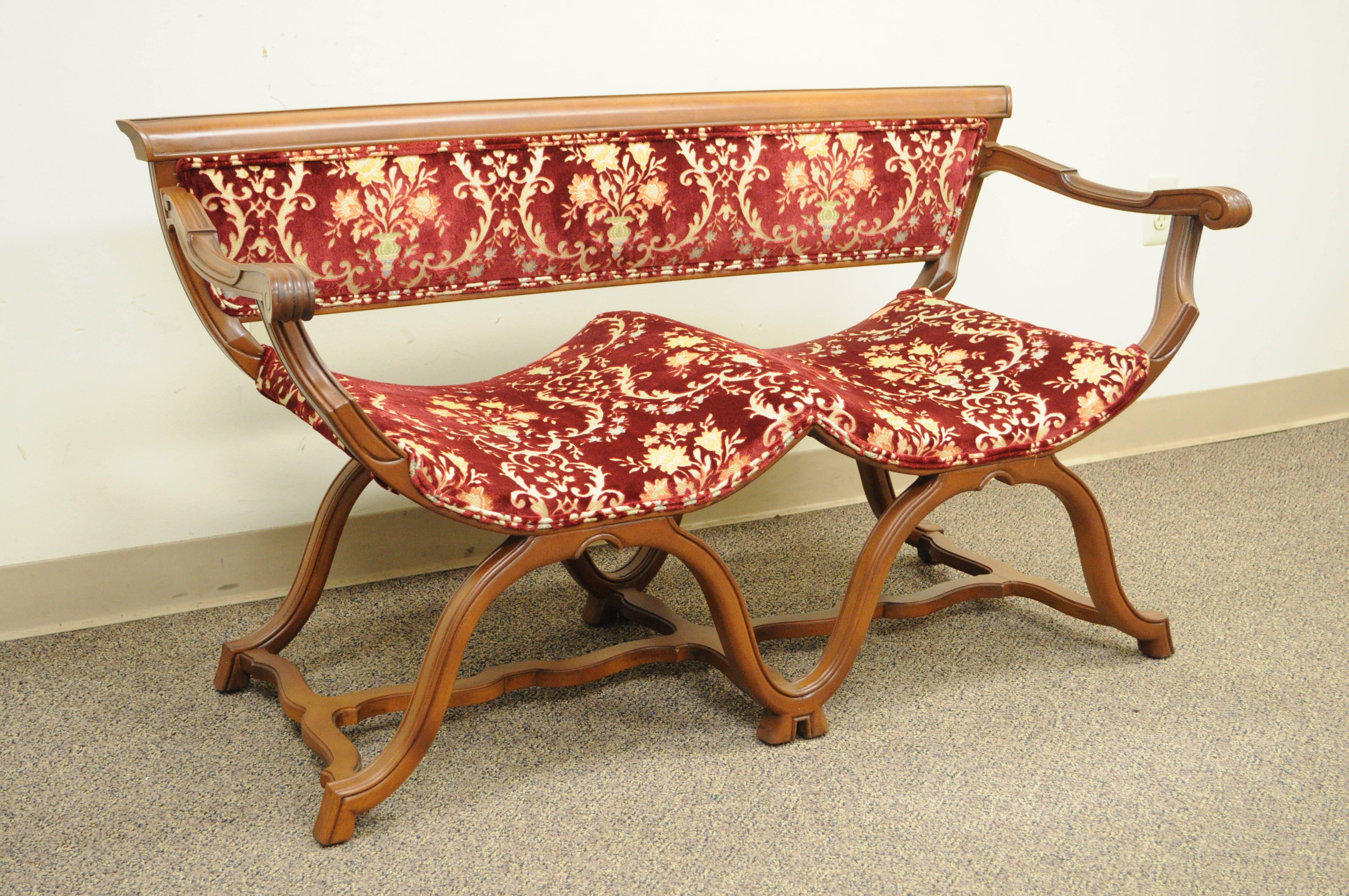 Unique vintage Hollywood Regency double Curule X-form Savonarola style bench. Item features a solid walnut carved wood frame, stretcher base, double curved seats, red textured floral printed upholstery, and great quality and construction.