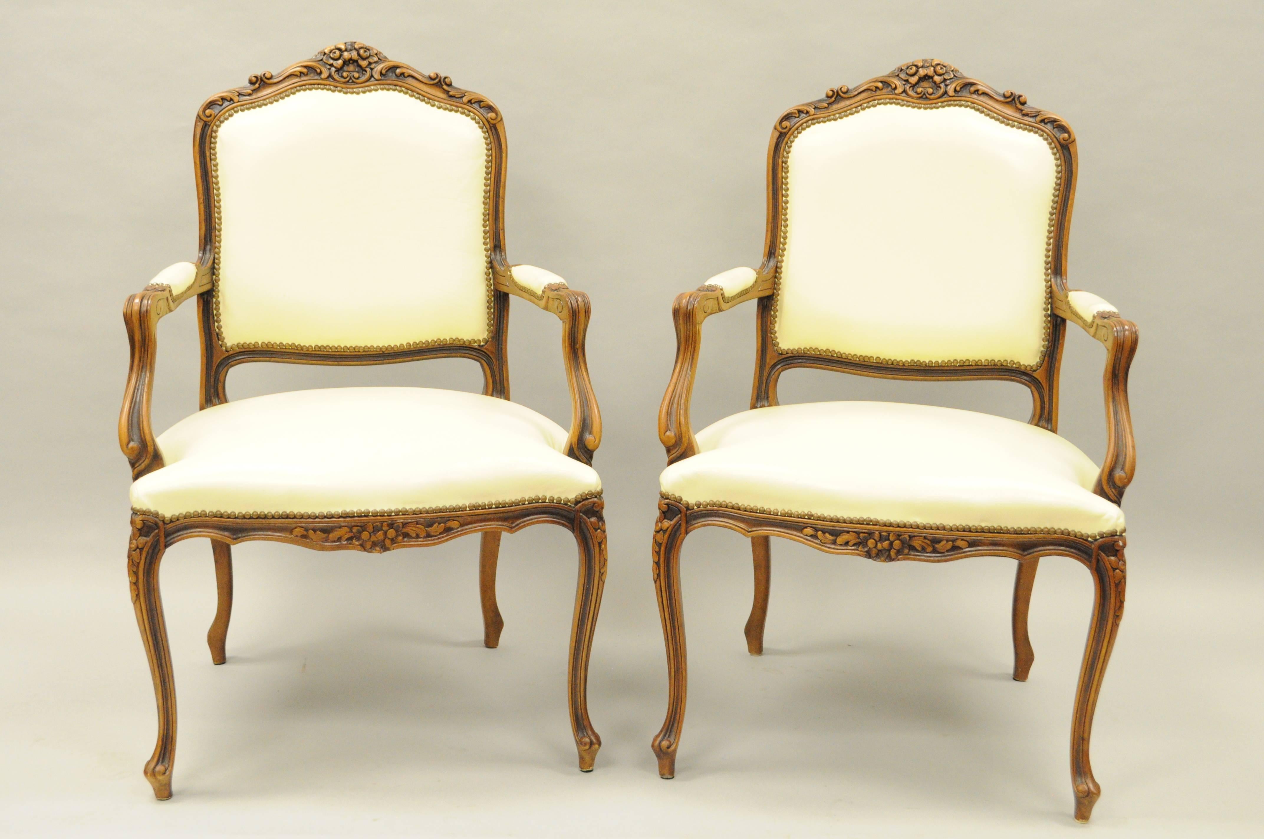 Pair of vintage Italian carved walnut French country or Louis XV style armchairs by Chateau d'Ax spa. Chairs feature cream colored leather upholstery, finely carved solid wood frames, upholstered armrests, nailhead trim, cabriole legs, and floral