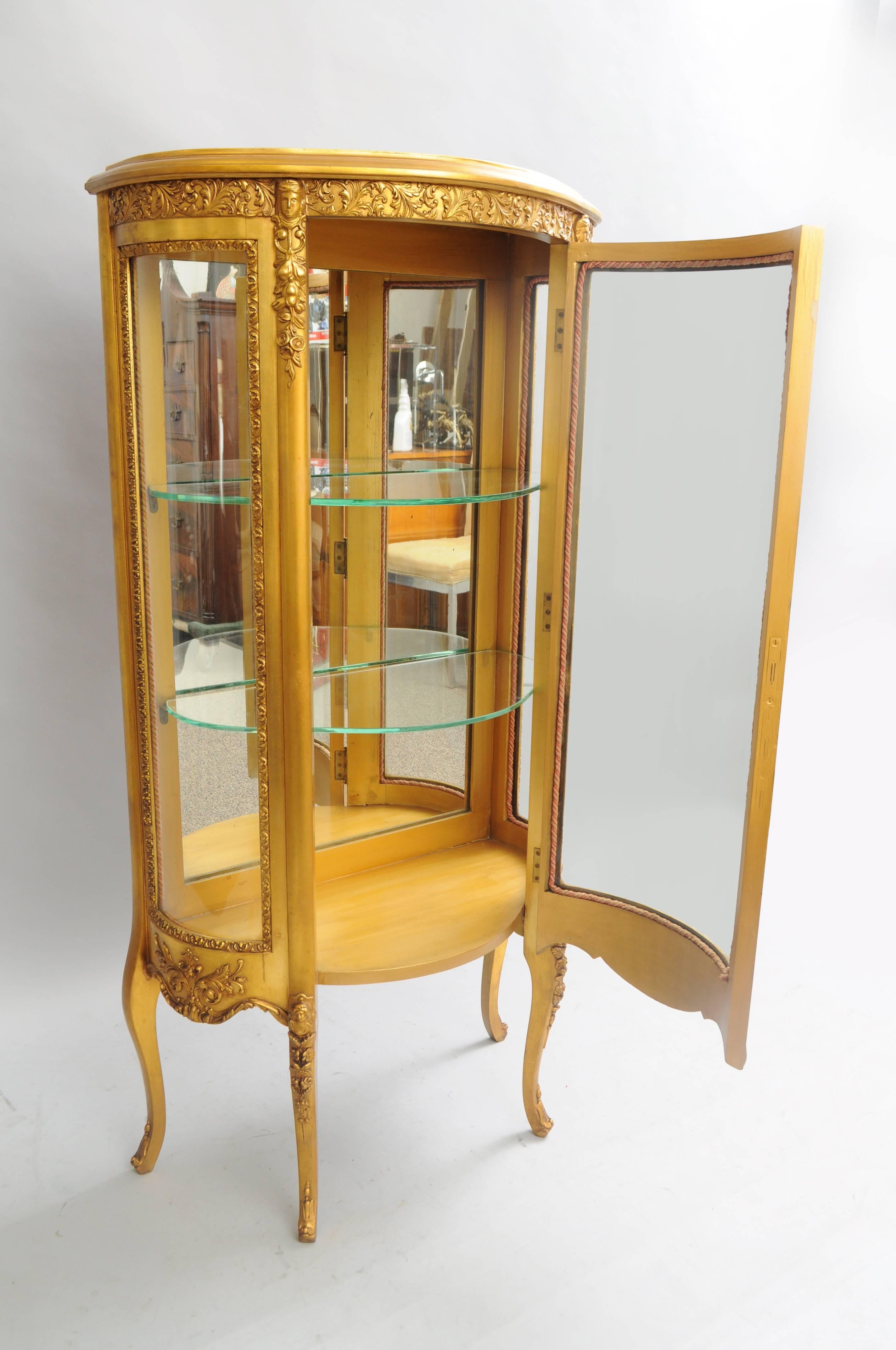 Small antique French Louis XV style gold giltwood curved glass figural display case. Item features a petite form with gold gilt acanthus detailing as well as faces on the upper and faces on the legs. Curio further features a single door with lock