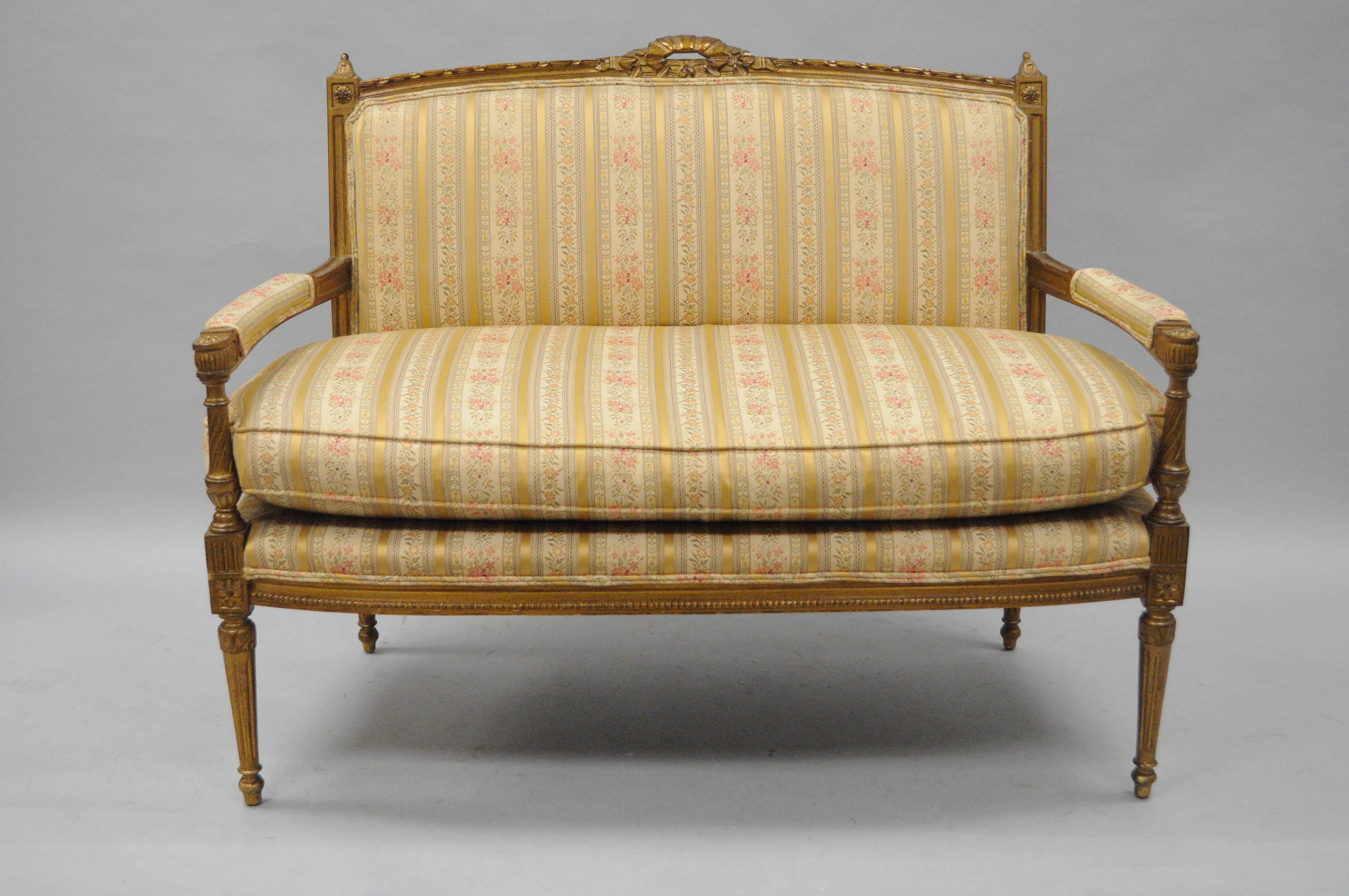 Vintage French Louis XVI style gold settee, circa mid-20th century. Settee features a ribbon carved crest, rectangular back, solid wood frame, upholstered armrests, gold striped fabric with pink floral print, reed and tapered legs, loose cushion,